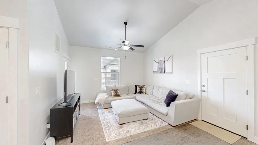 Vaulted ceiling living room featuring a ceiling fan, a multi-pane window, and a three-panel interior door