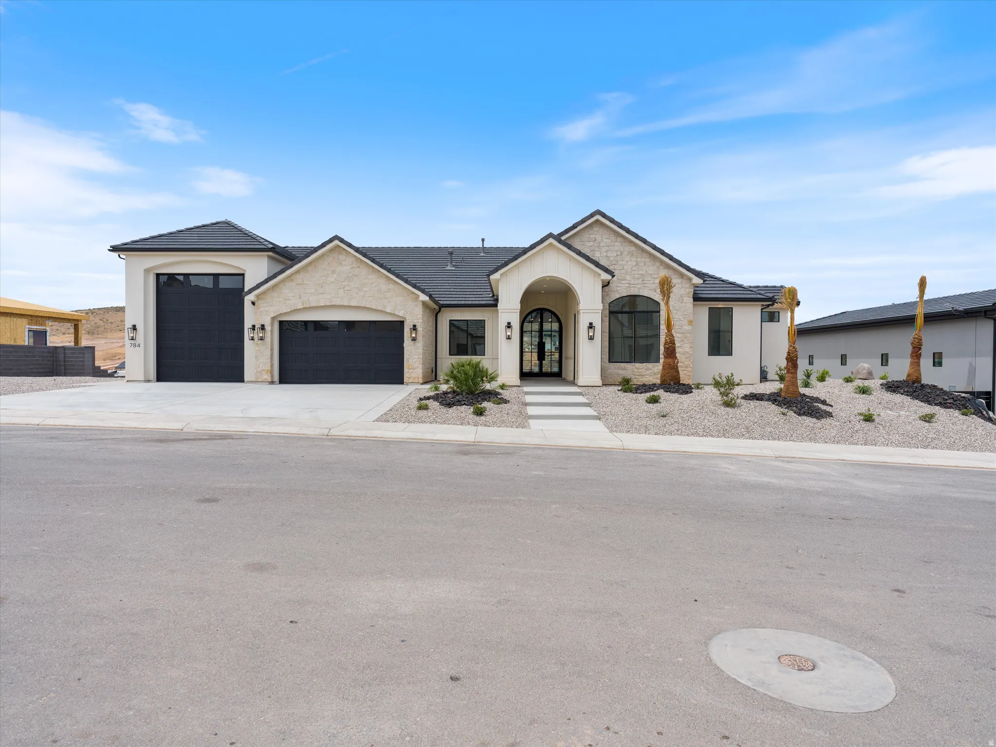 Contemporary stucco and stone exterior featuring a dark tile roof and arched entry