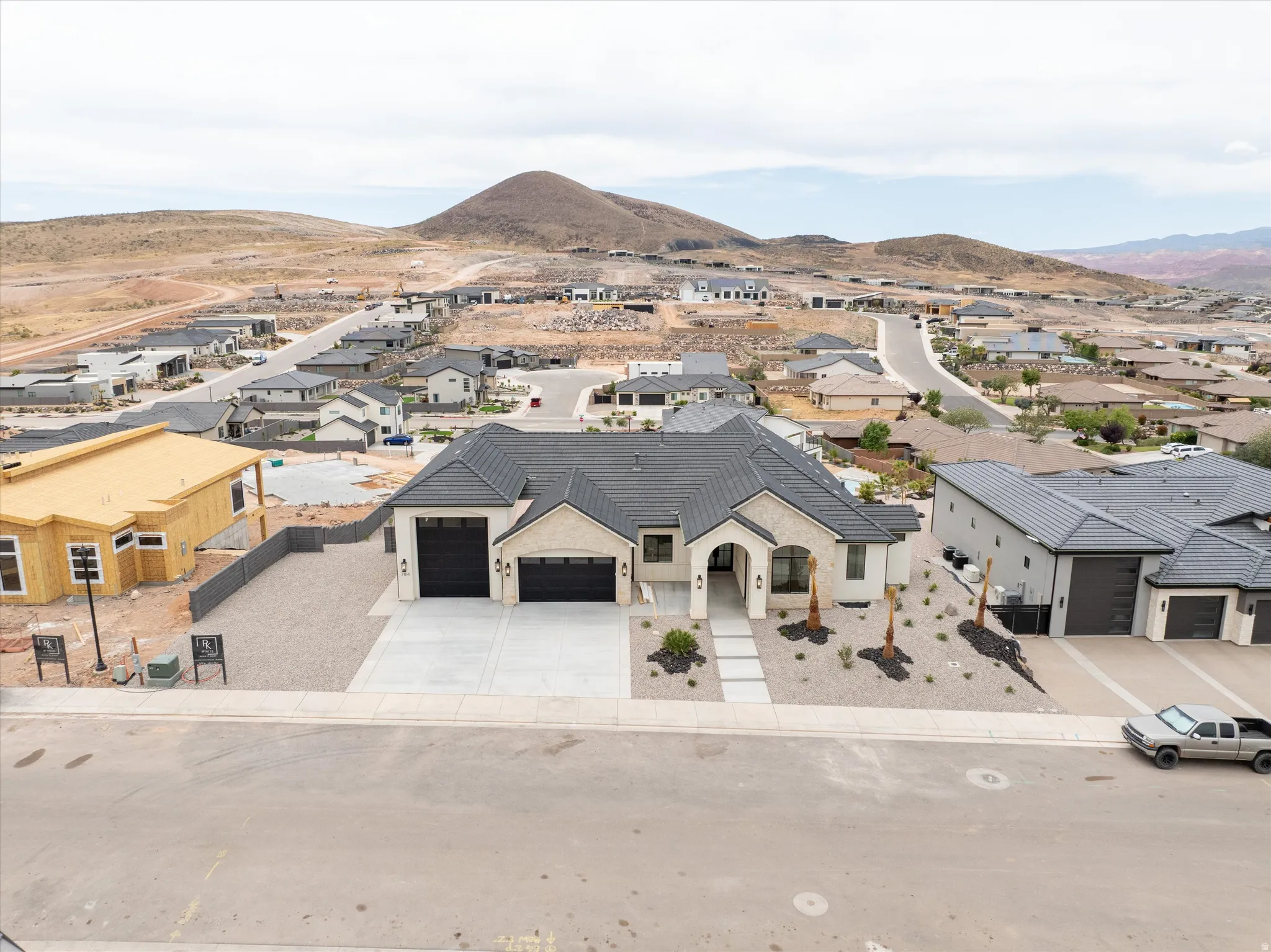 Modern residence featuring a light-colored stucco and stone facade, dark tile roofing, and two black garage doors
