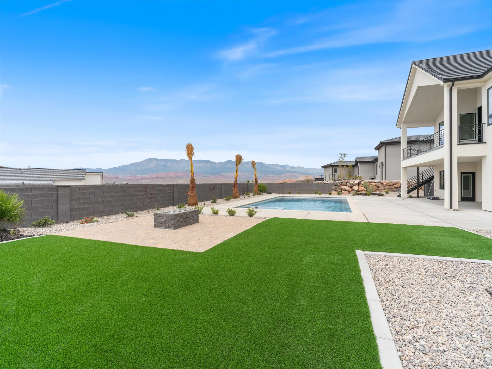 Expansive backyard featuring a rectangular swimming pool, artificial turf, and a paver patio with a built-in fire pit