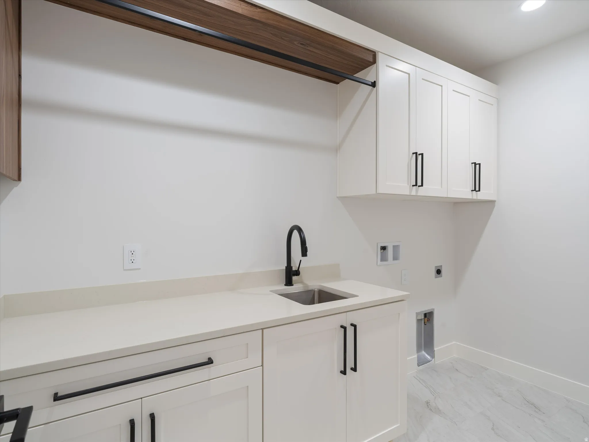 Laundry area featuring white cabinetry with black hardware, a light-toned countertop, and a stainless steel sink with a matte black faucet