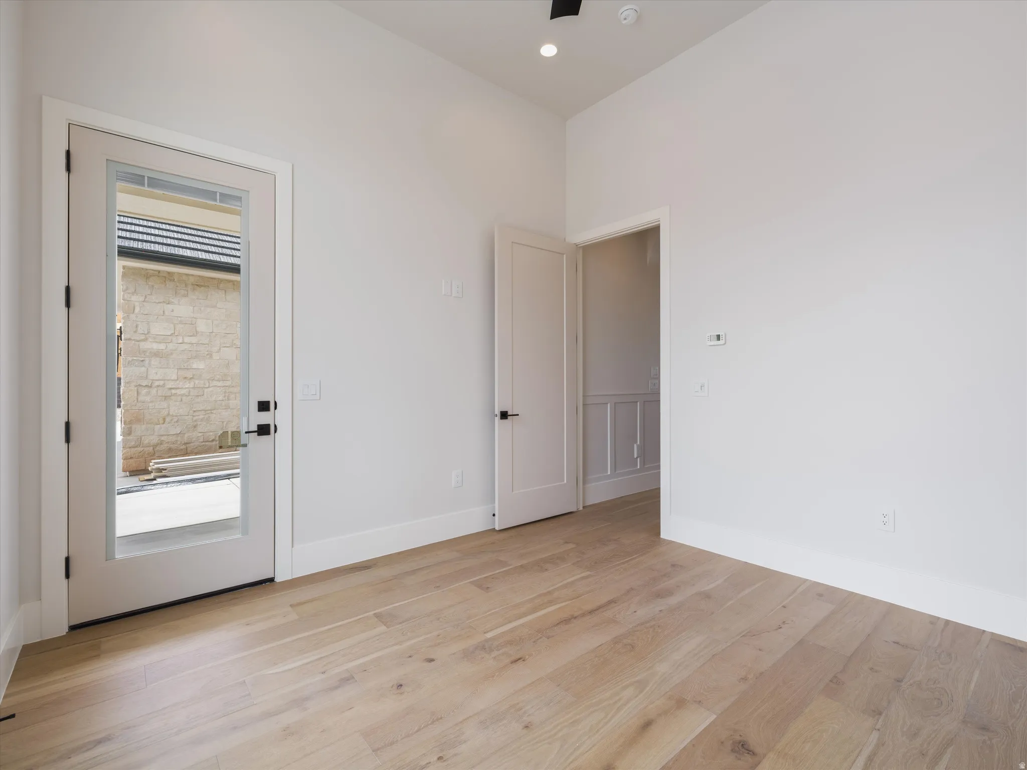 Spacious room featuring wood-finish flooring, white baseboards, and a glass-paneled exterior door with matte black hardware