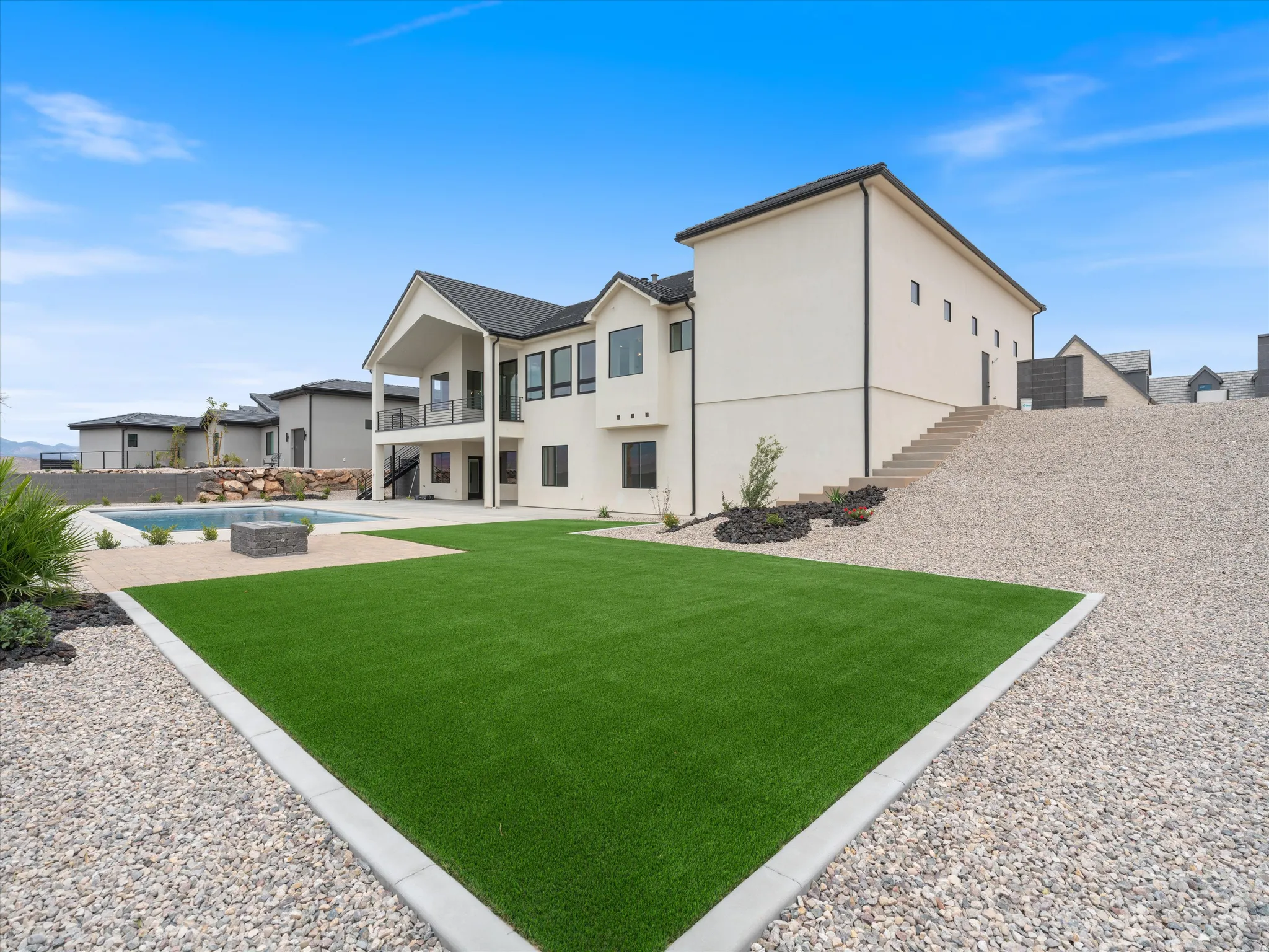 Expansive outdoor area featuring artificial turf, gravel landscaping, a built-in swimming pool, a fire pit, and a multi-level patio