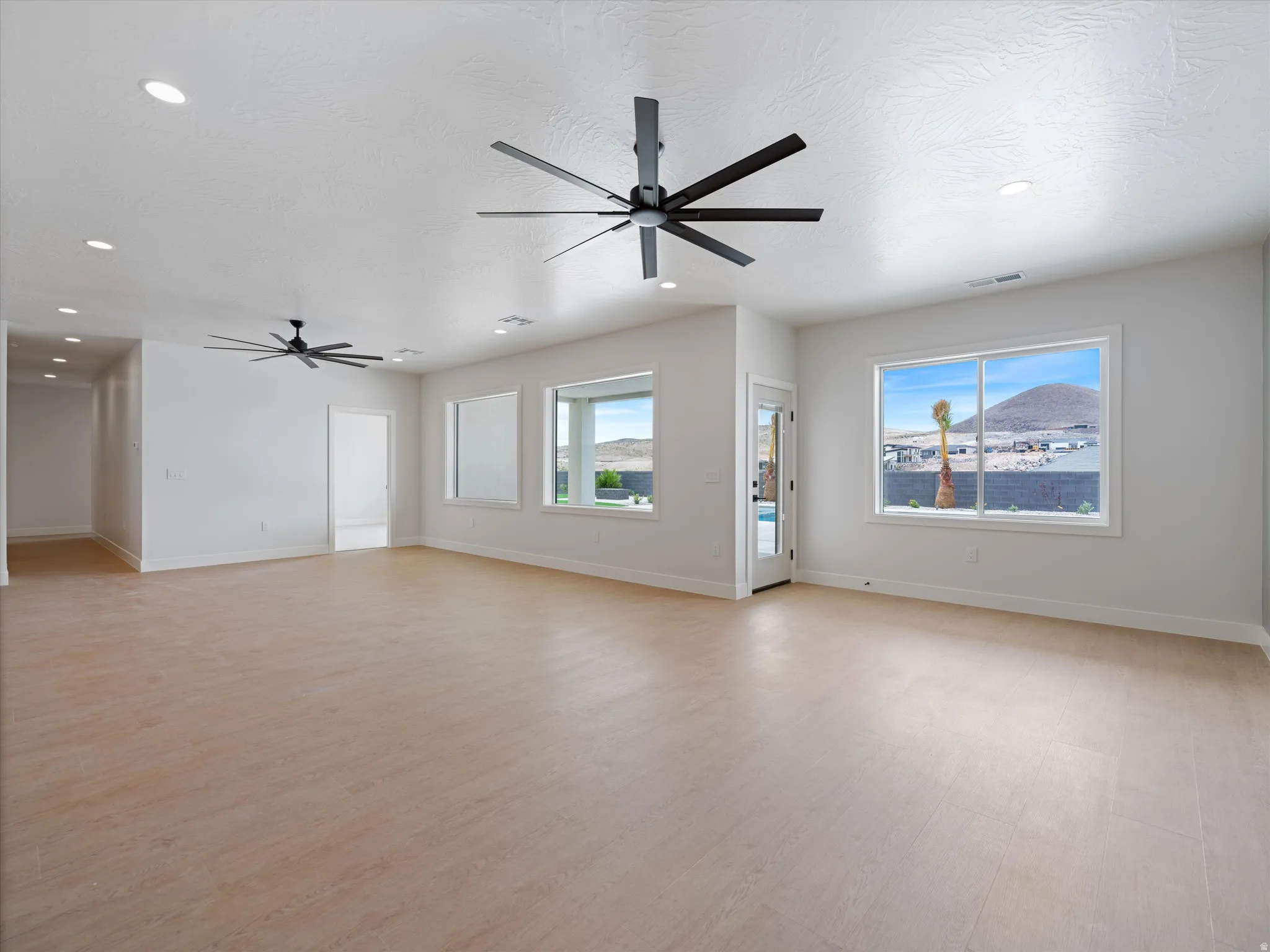 Spacious interior living area featuring light wood-finish flooring, recessed lighting, and multiple large windows