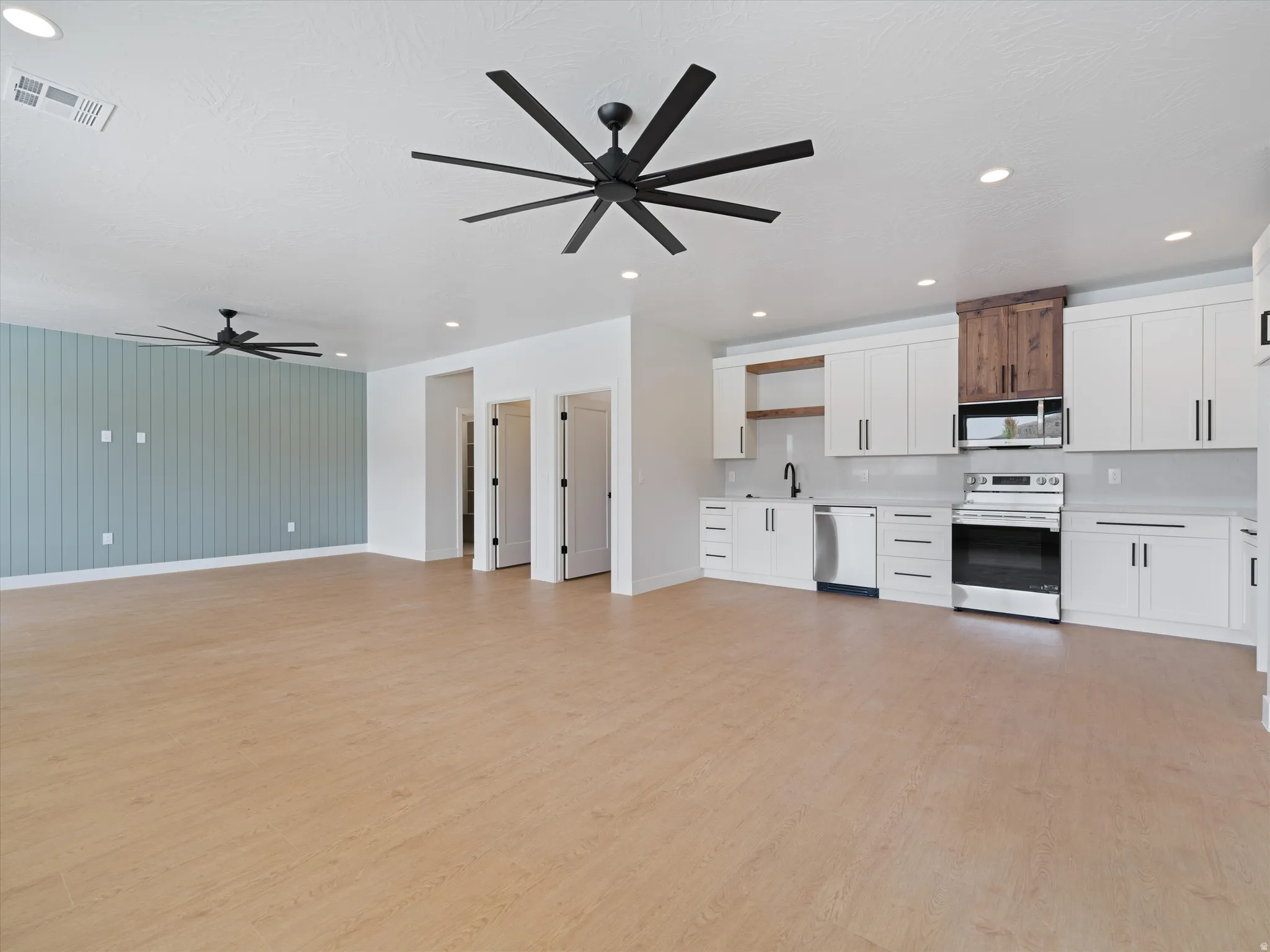 Open-concept living space featuring wood-finish flooring, recessed lighting, and two multi-blade ceiling fans