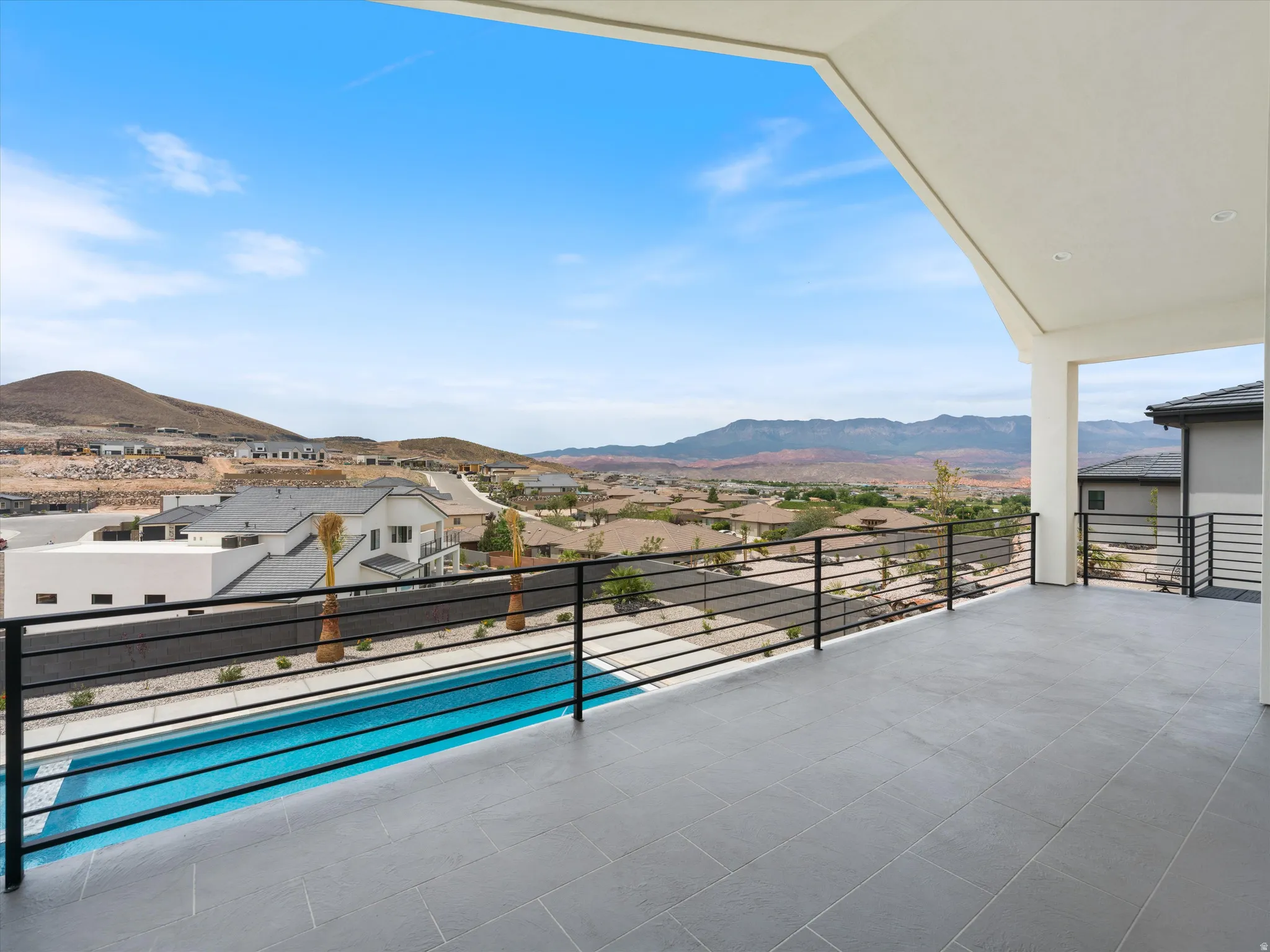 Spacious outdoor patio with large format tile flooring, black metal railing, and a private swimming pool