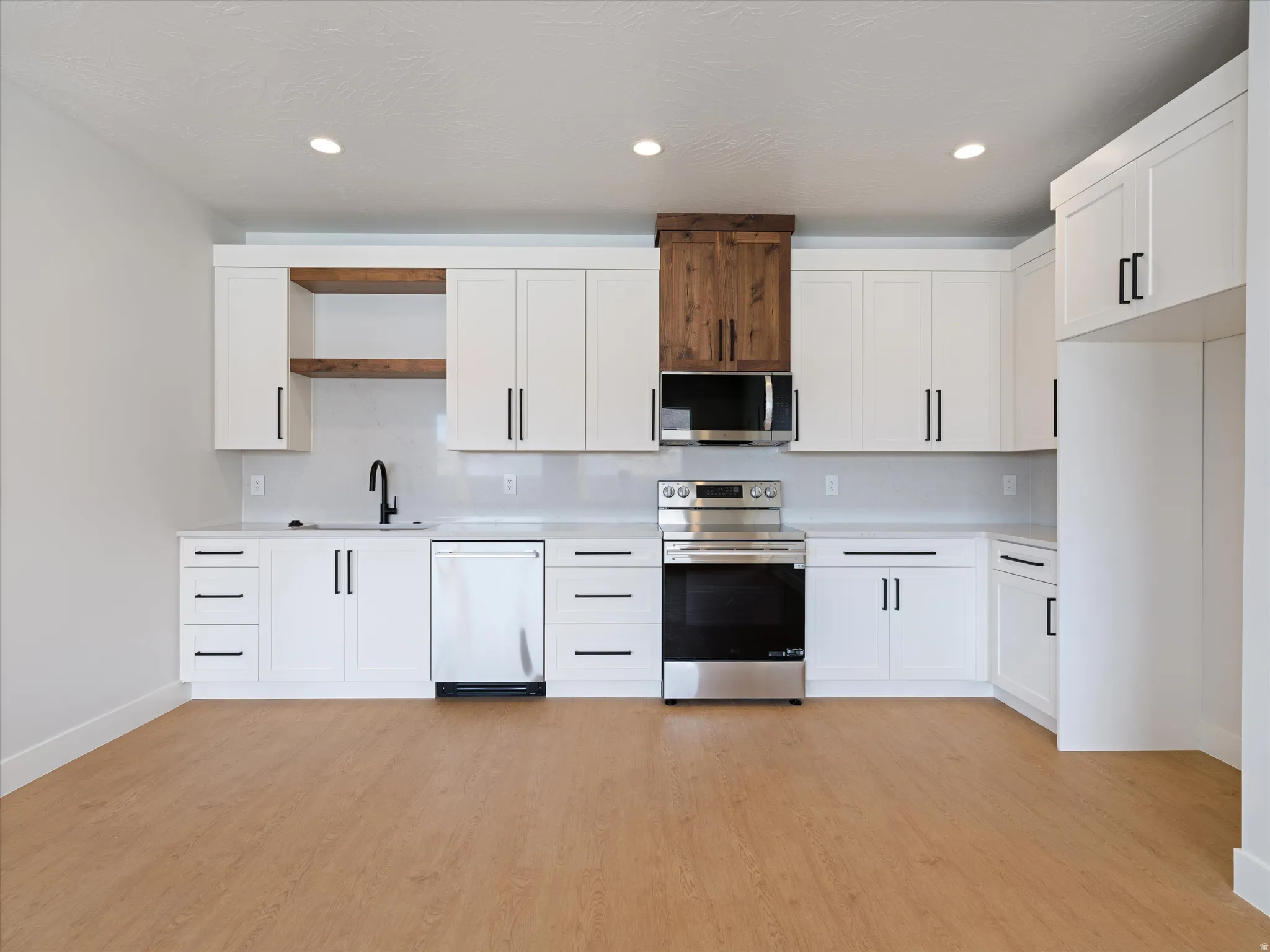 Modern kitchen featuring white cabinetry with contrasting black hardware, stainless steel appliances, and wood-finish flooring