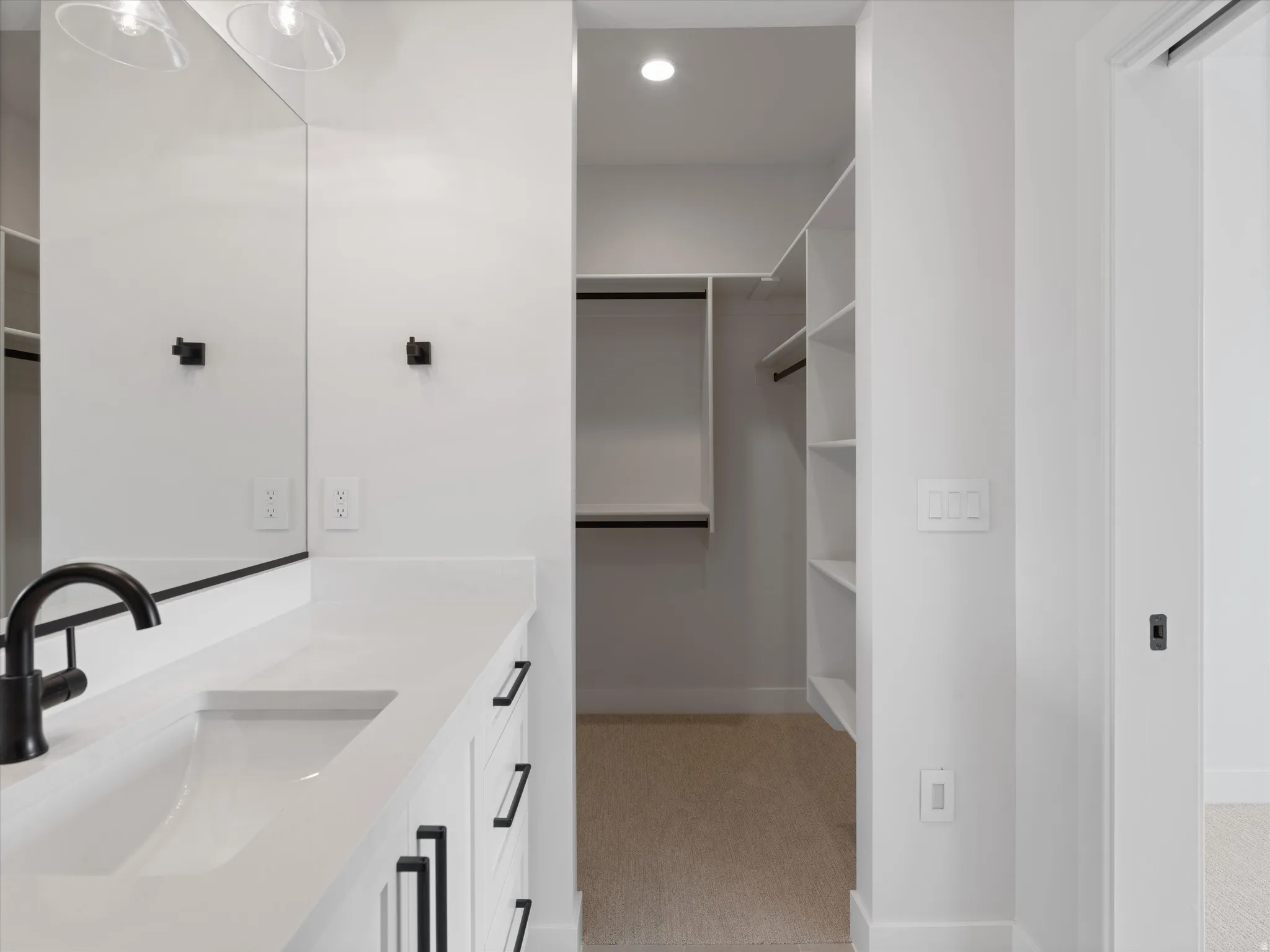 Contemporary bathroom vanity with a white countertop and integrated sink, matte black faucet, and white cabinetry featuring black hardware