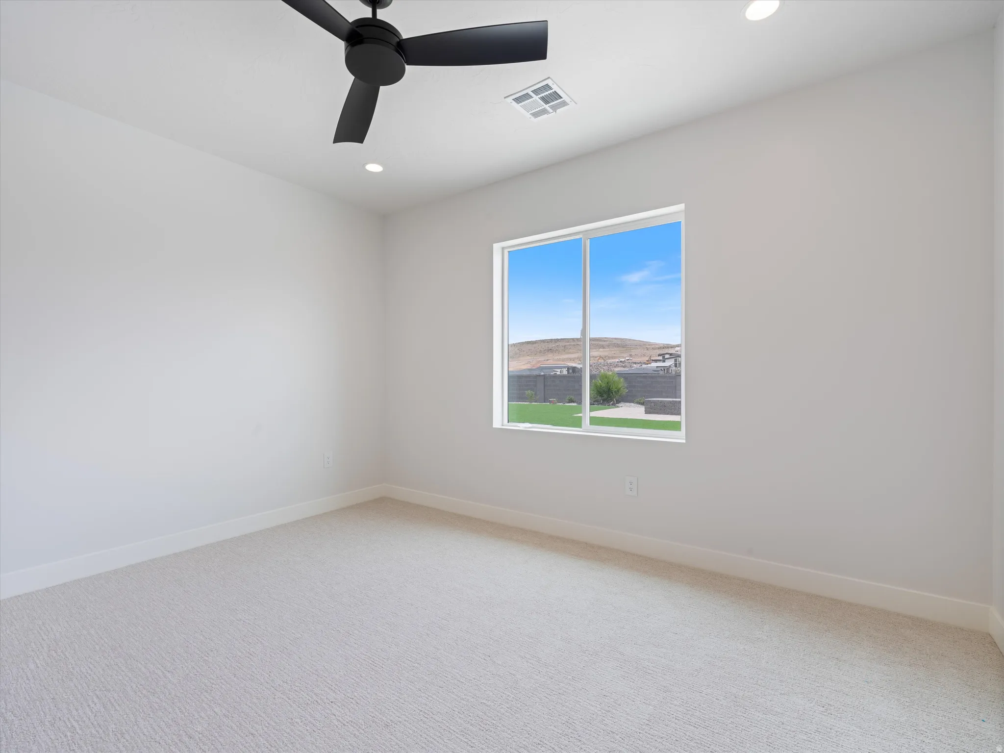 Light-filled room featuring a single window, recessed lighting, a modern black ceiling fan, white baseboards, and light-colored carpet flooring