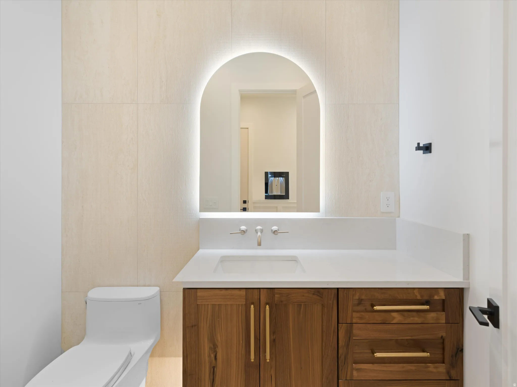 Vanity featuring a light wood-finish cabinet with gold-tone hardware, white countertop, and integrated sink