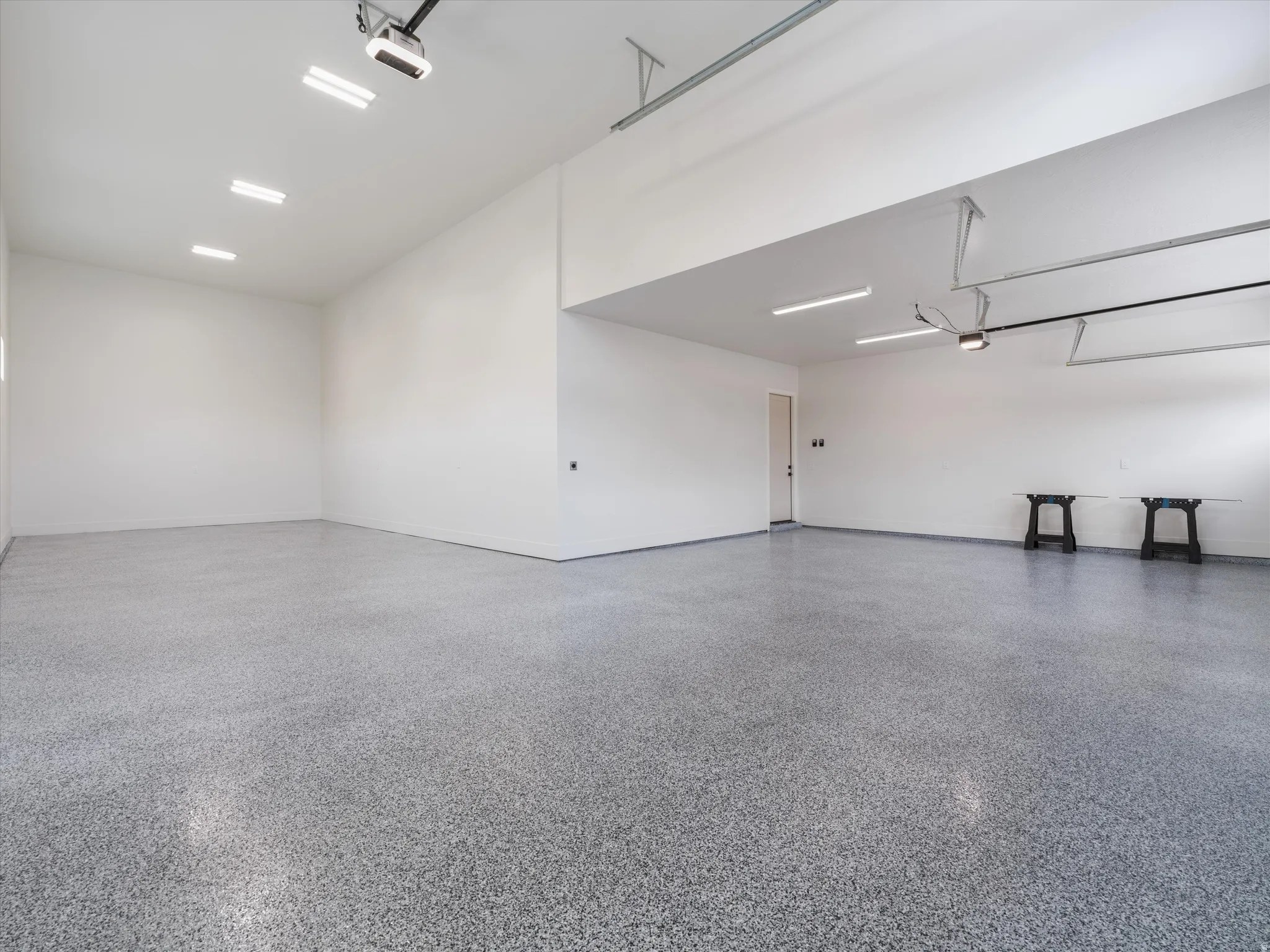 Spacious garage featuring a speckled epoxy floor, white painted walls, recessed lighting, and an overhead garage door opener mechanism