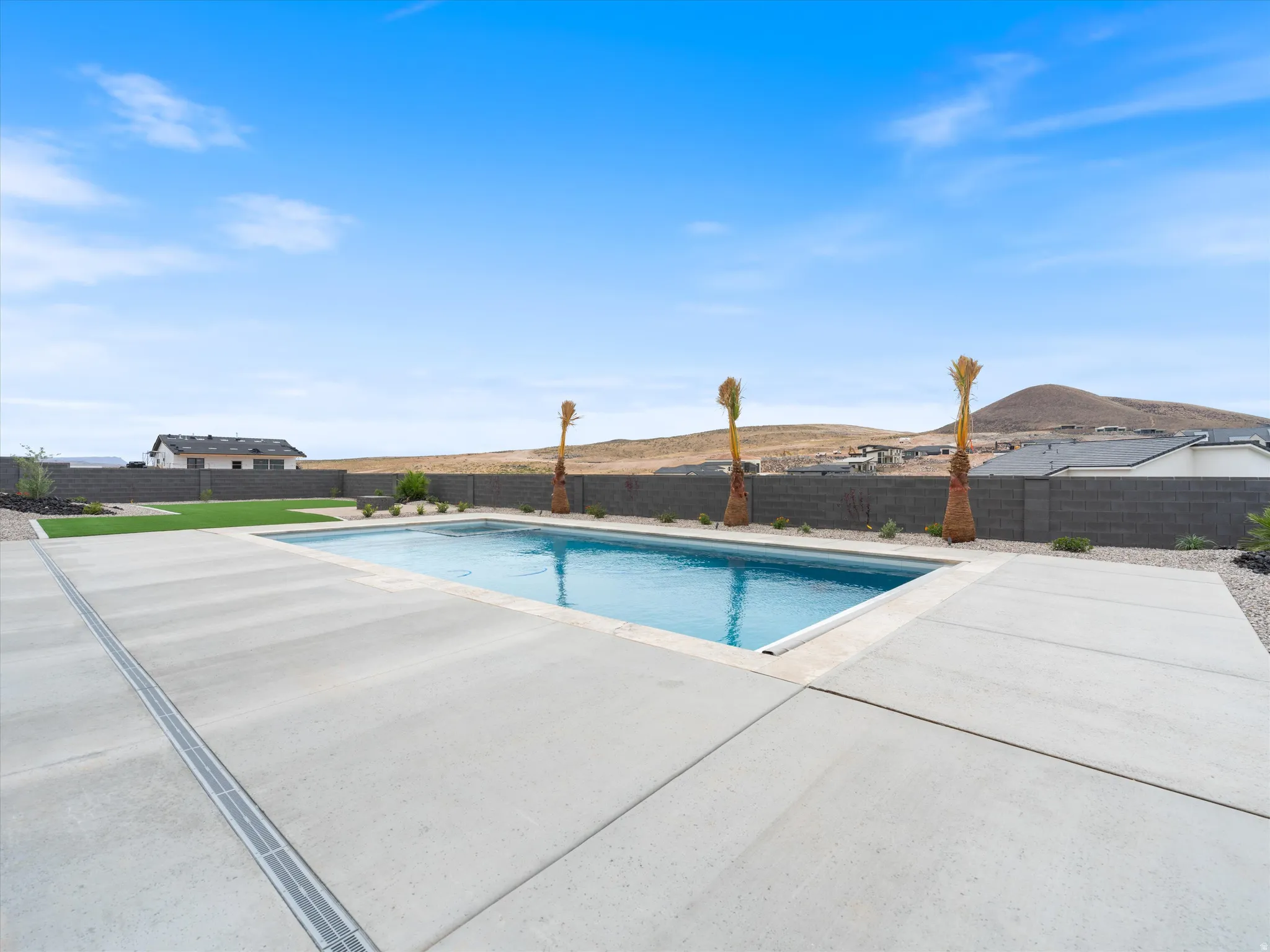 Expansive outdoor living area featuring a rectangular swimming pool, concrete decking, and artificial turf
