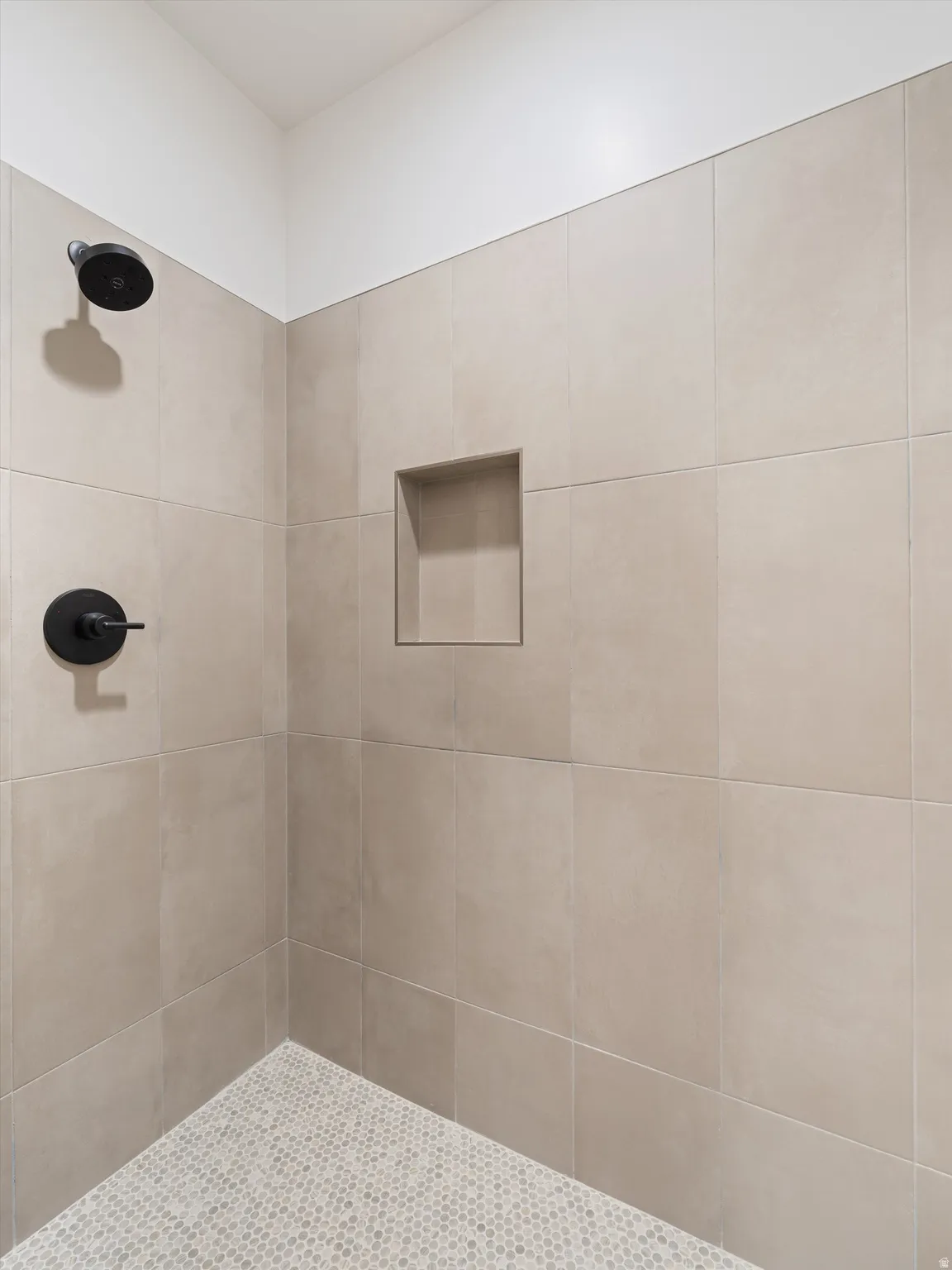 Tiled shower enclosure featuring light-toned large format wall tiles and a mosaic tile floor