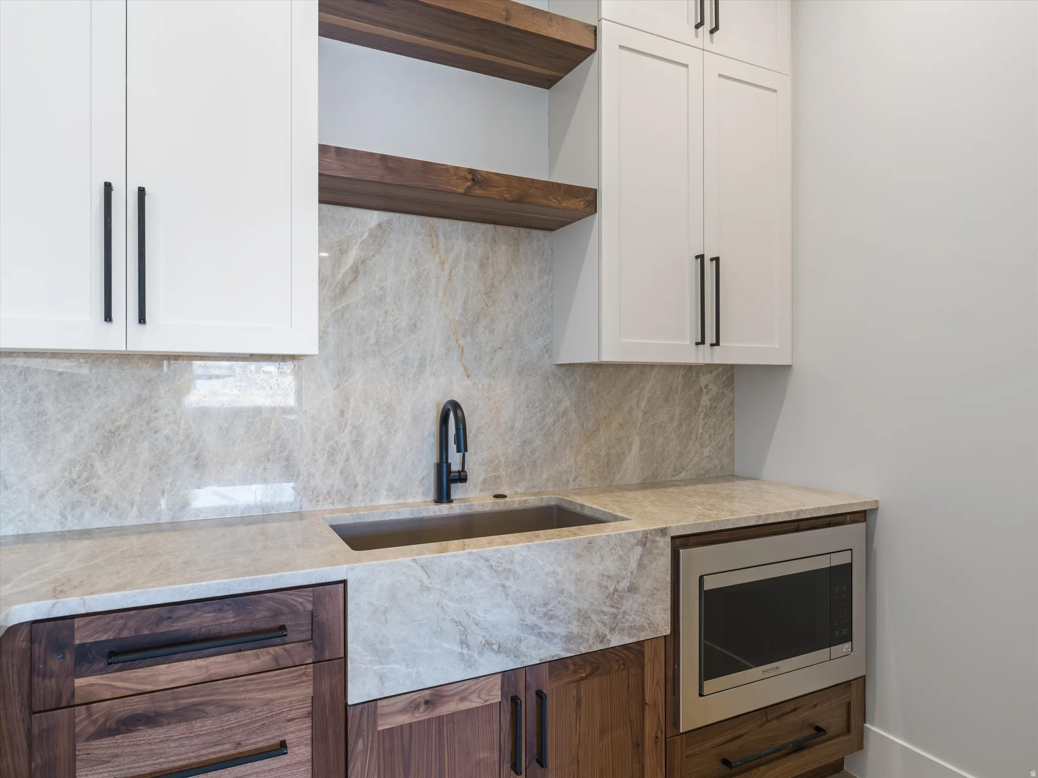 Built-in stainless steel microwave, stone countertop, matte black faucet, and a stone farmhouse sink