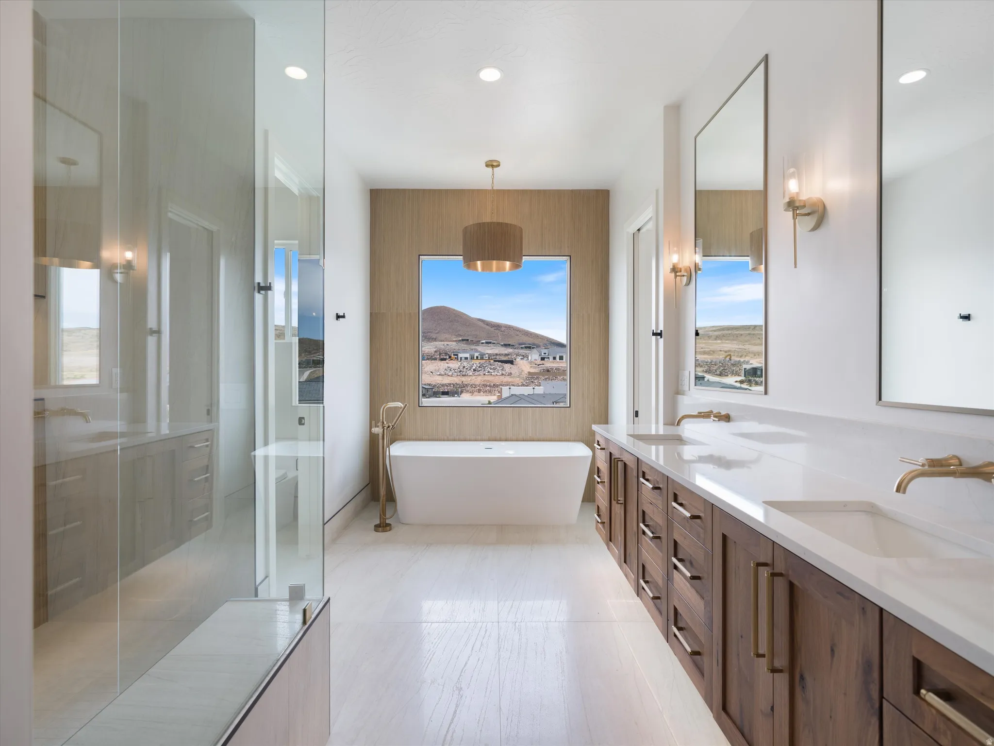 Spacious bathroom with a freestanding soaking tub, dual vanities featuring wood cabinetry and white countertops, a glass-enclosed shower, and light wood-finish flooring