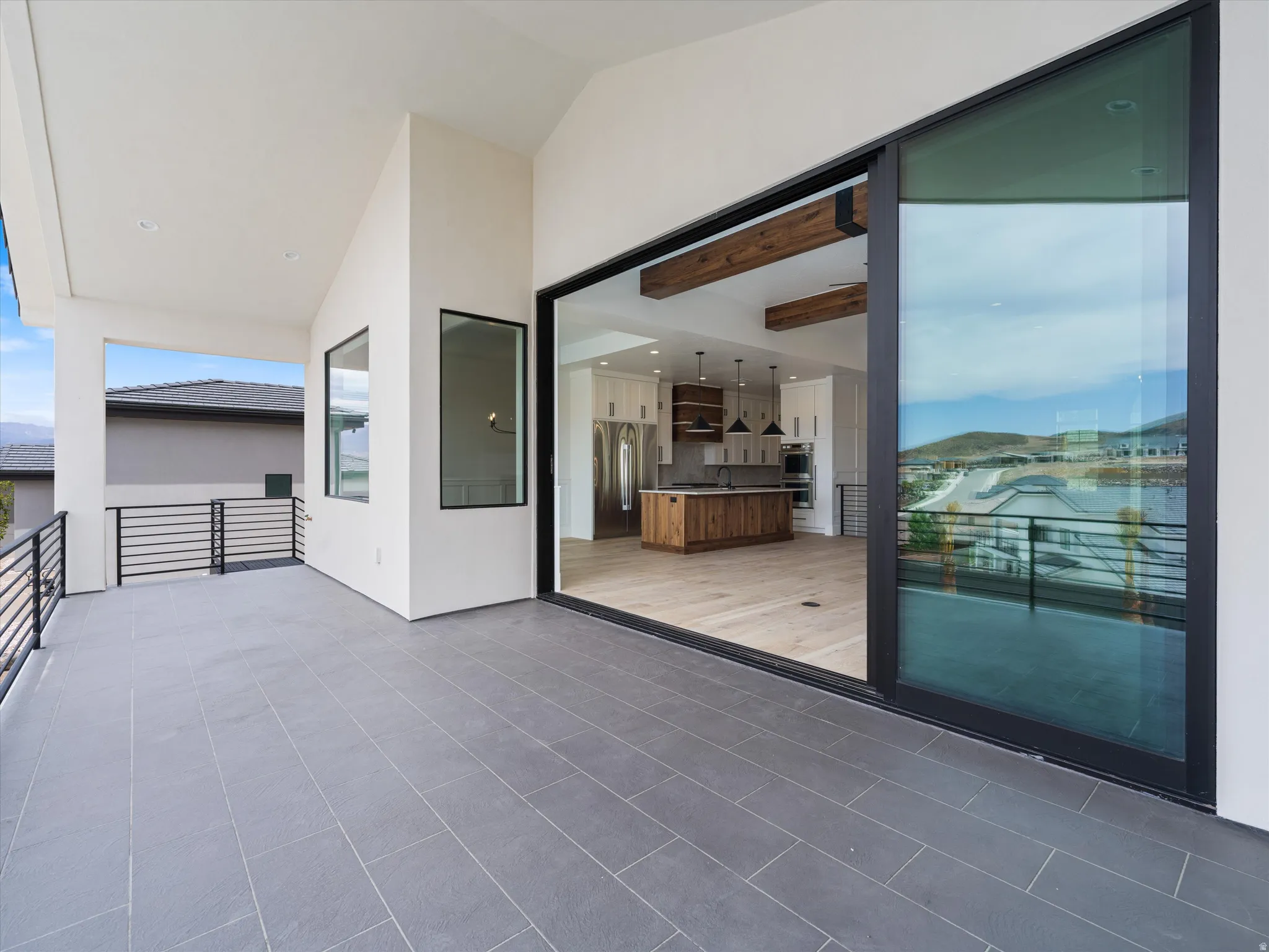 Expansive covered outdoor living space featuring dark gray rectangular tile flooring and black metal railing