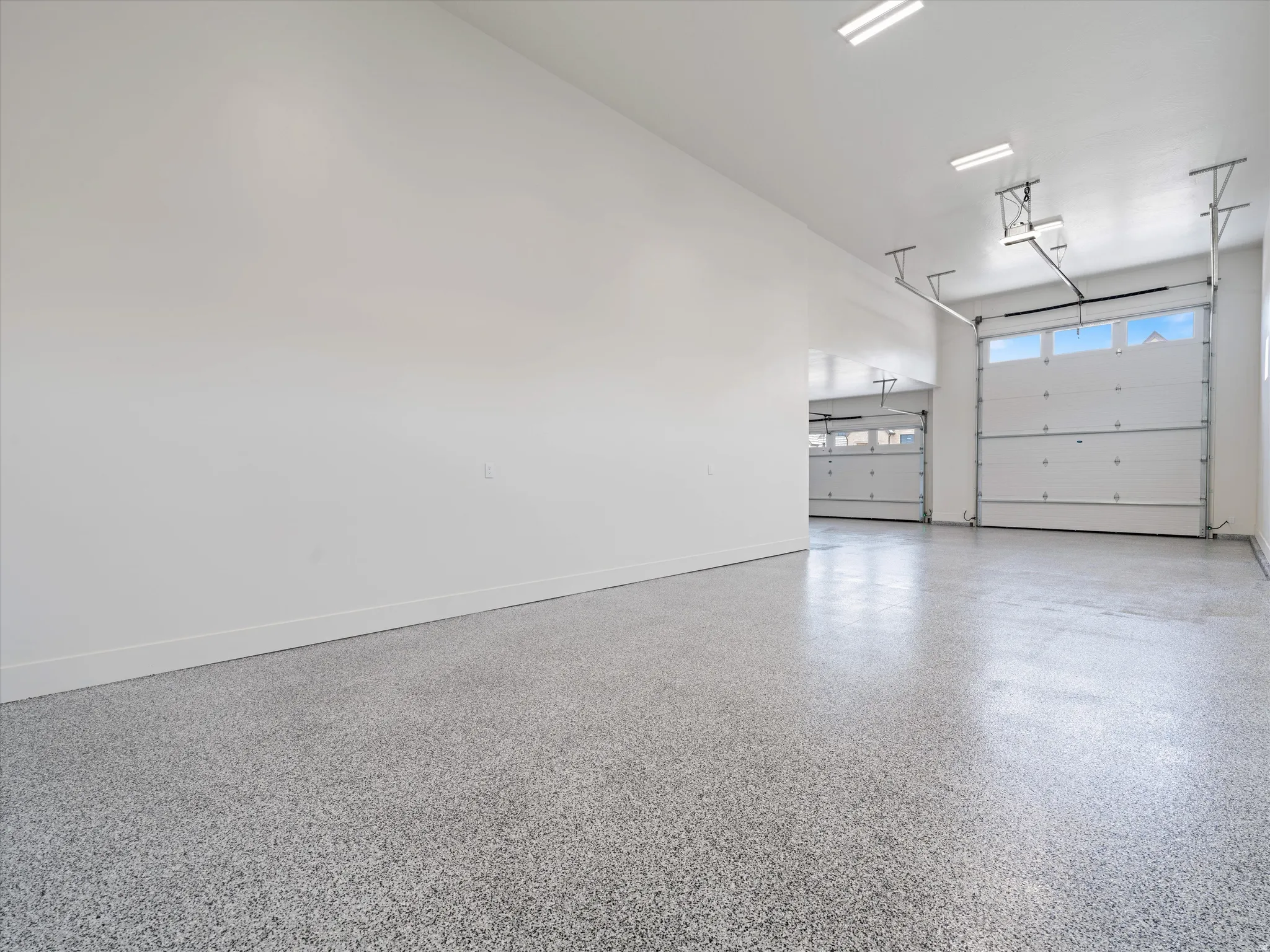 Expansive garage featuring a speckled epoxy floor, multiple overhead garage doors with window panels, and fluorescent lighting fixtures