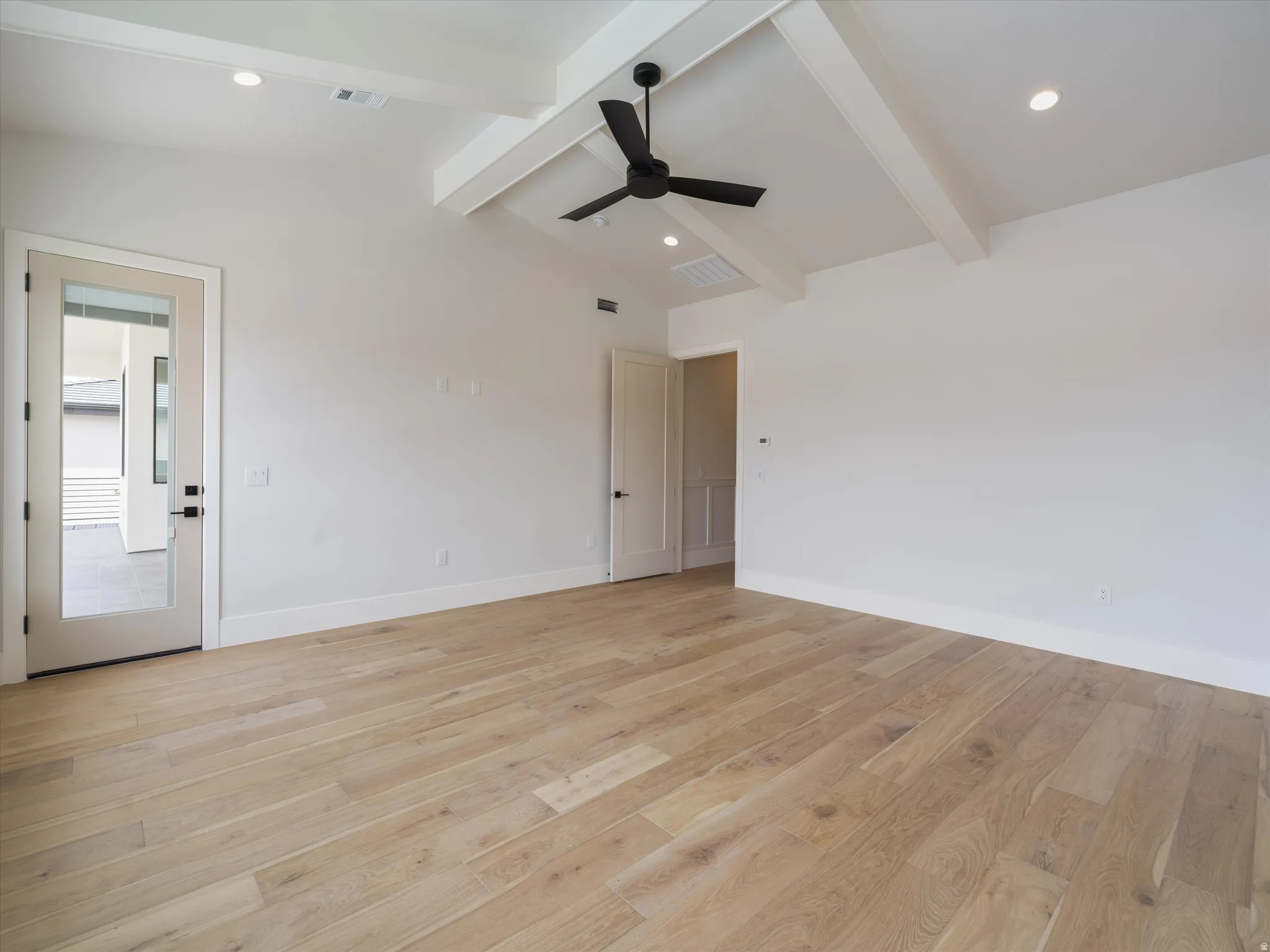 Spacious room featuring light wood-finish flooring and a vaulted ceiling with exposed beams