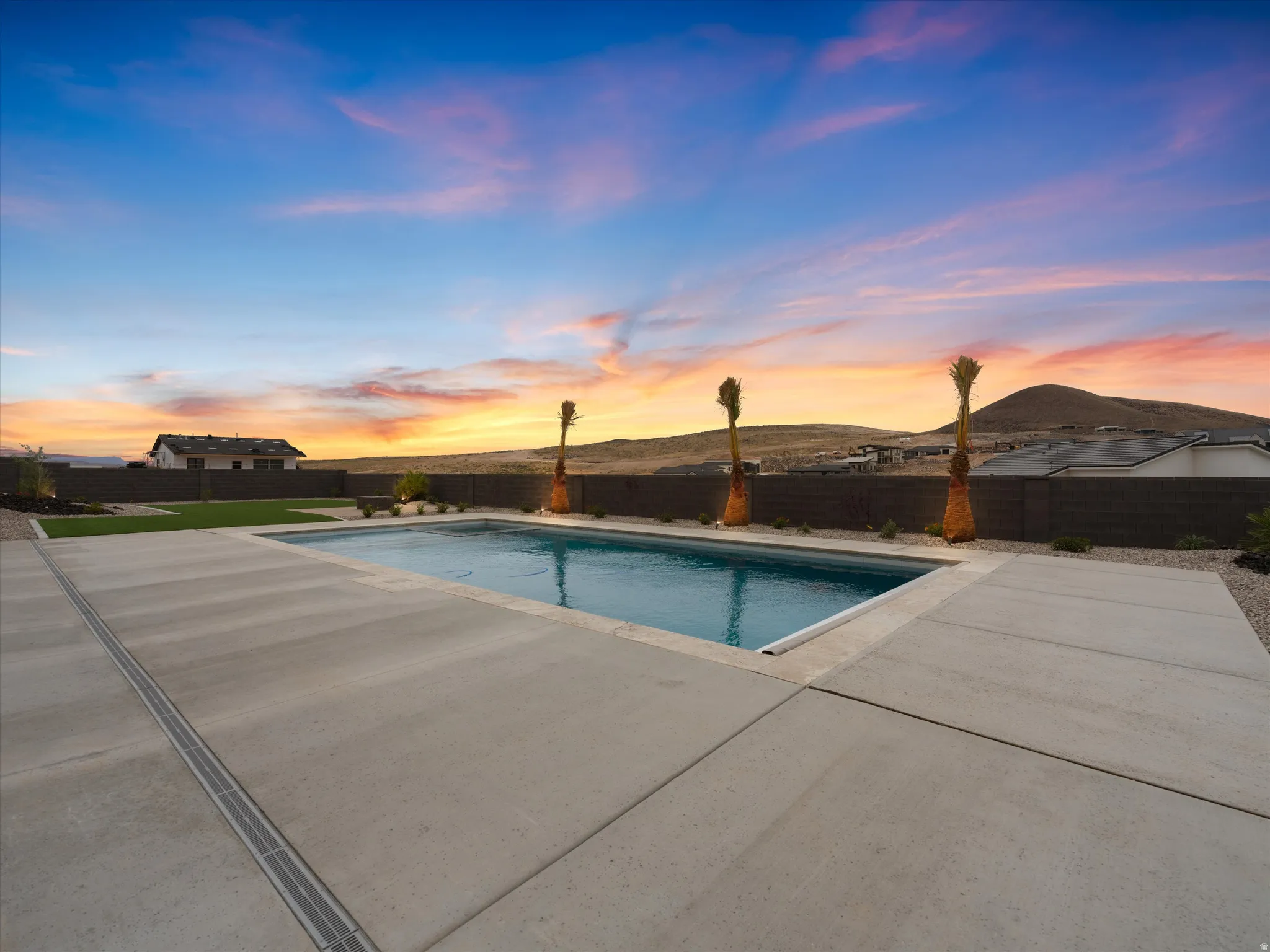 Rectangular swimming pool with extensive concrete decking, surrounded by artificial turf and desert landscaping