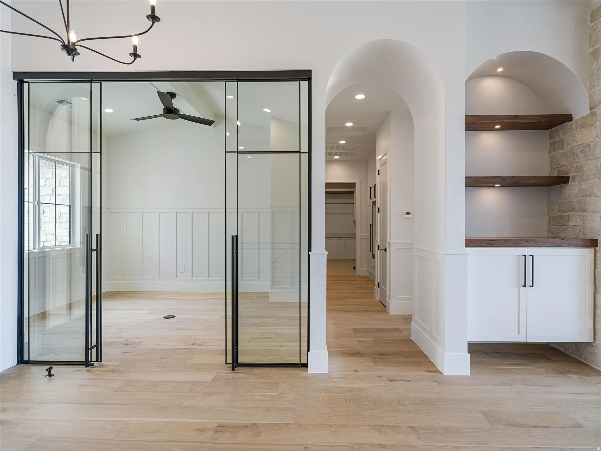 Glass-paneled entry doors with matte black framing open to a room featuring wood-finish flooring and wainscoting