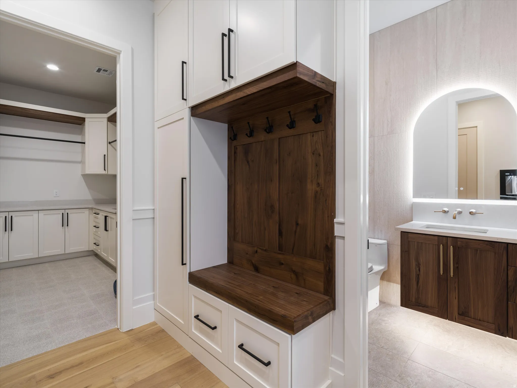 Built-in mudroom with rich wood-finish bench, coat hooks, and integrated white cabinetry
