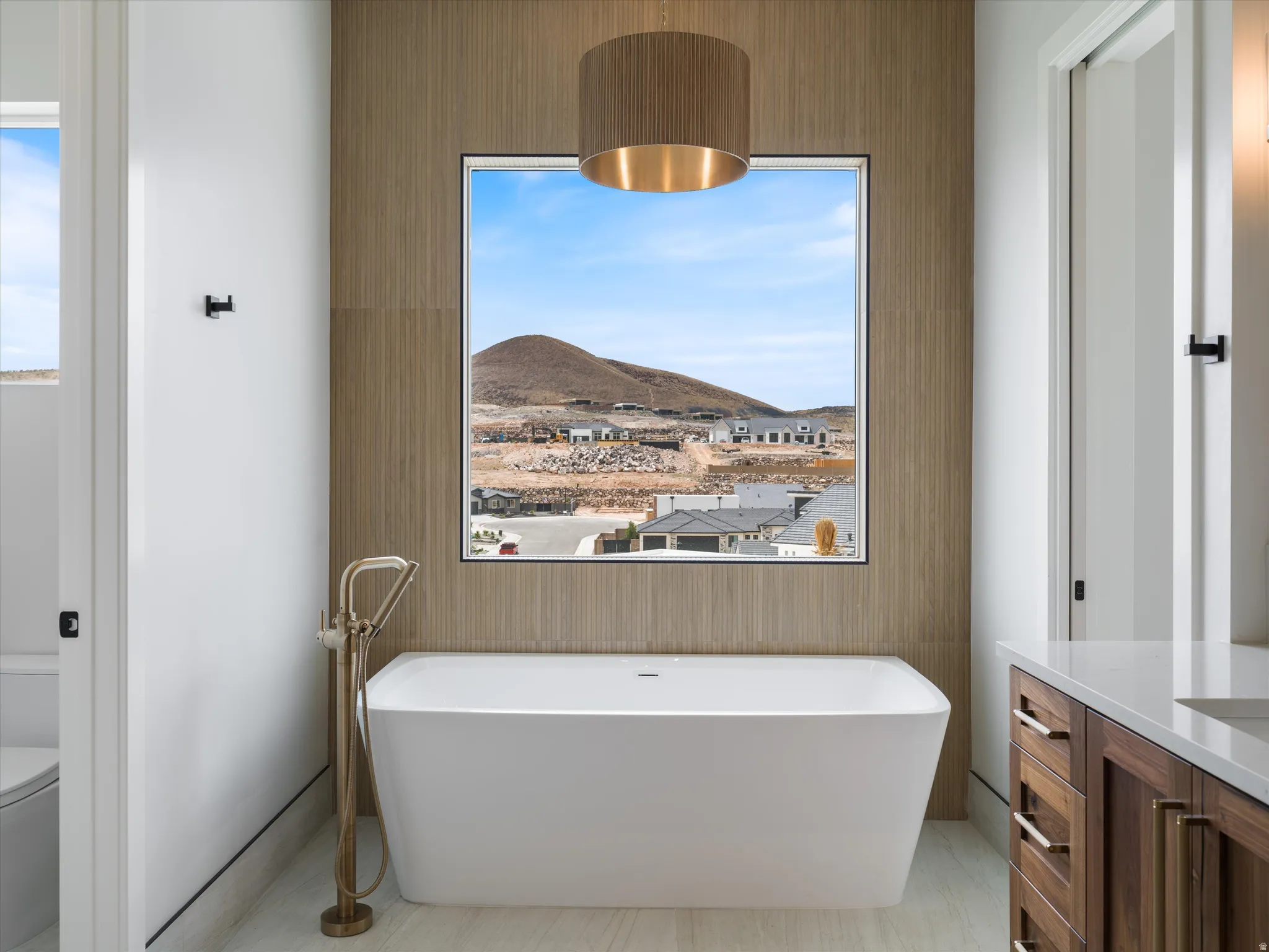Freestanding soaking tub with a floor-mounted gold-tone faucet, set against a wood-panel accent wall