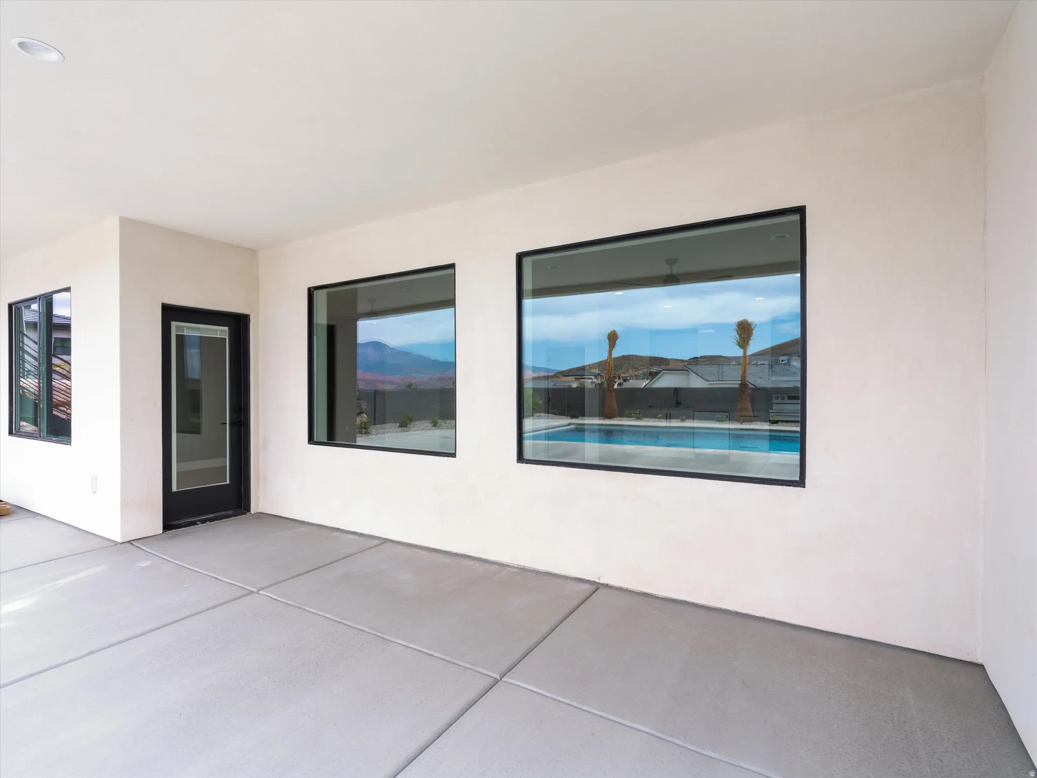 Spacious patio featuring concrete flooring, a black-framed glass door, and large black-framed windows overlooking a swimming pool and distant mountains