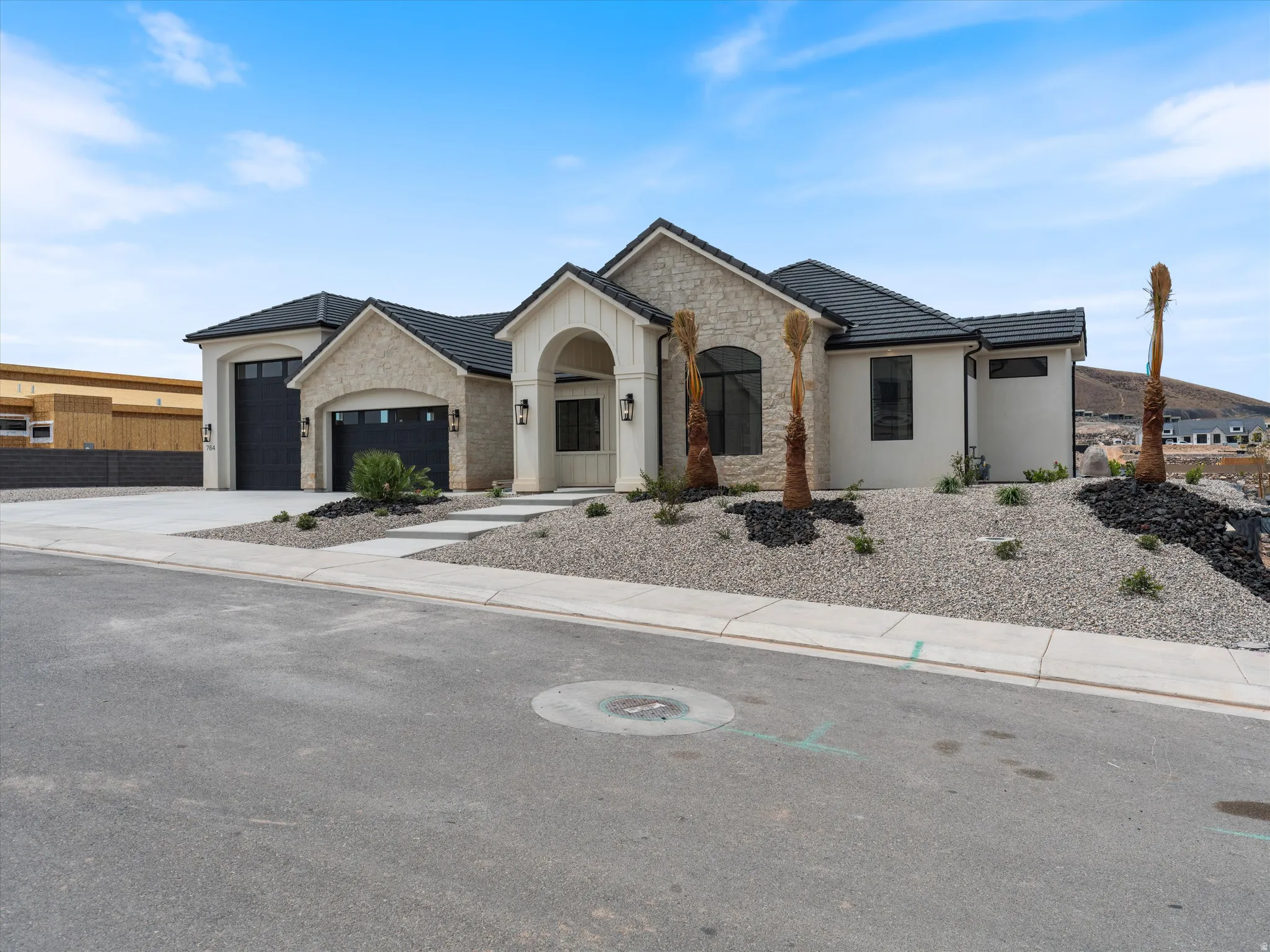 Contemporary stucco exterior with stone accents, a dark tile roof, and multiple garage doors