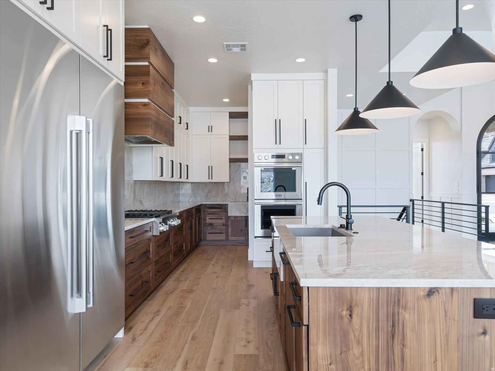 Gourmet kitchen featuring a large central island with an undermount sink, stainless steel appliances, wood-finish flooring, and two-tone cabinetry with black hardware