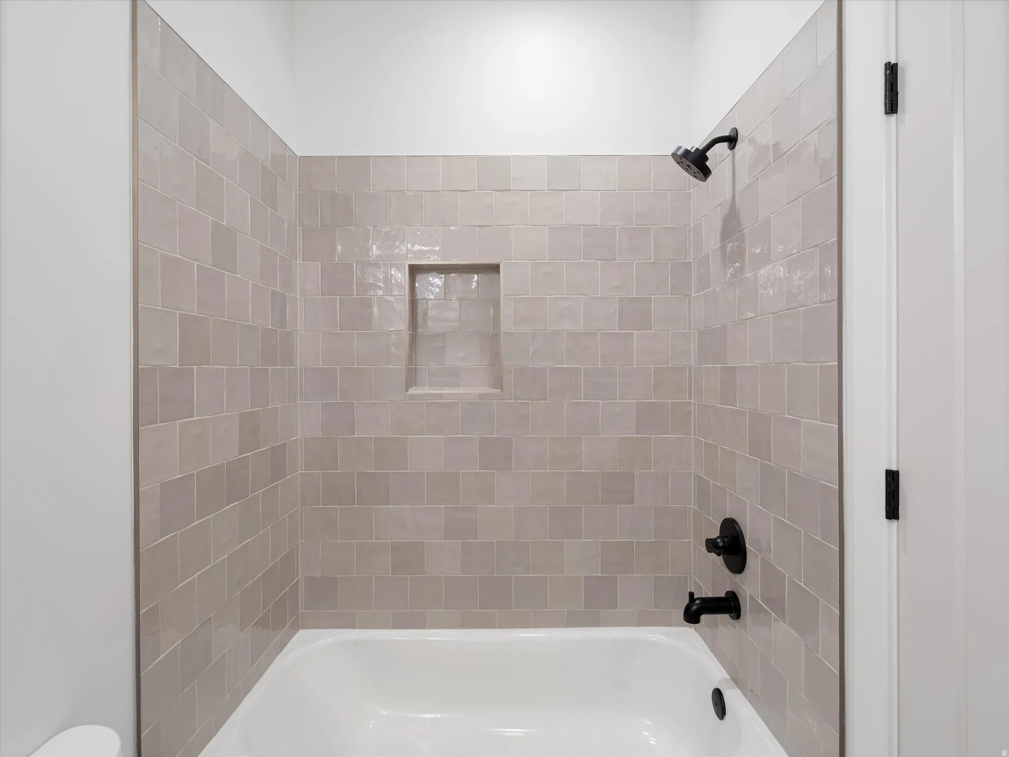 Bathtub with light-toned square wall tiles, a recessed shower niche, and matte black fixtures