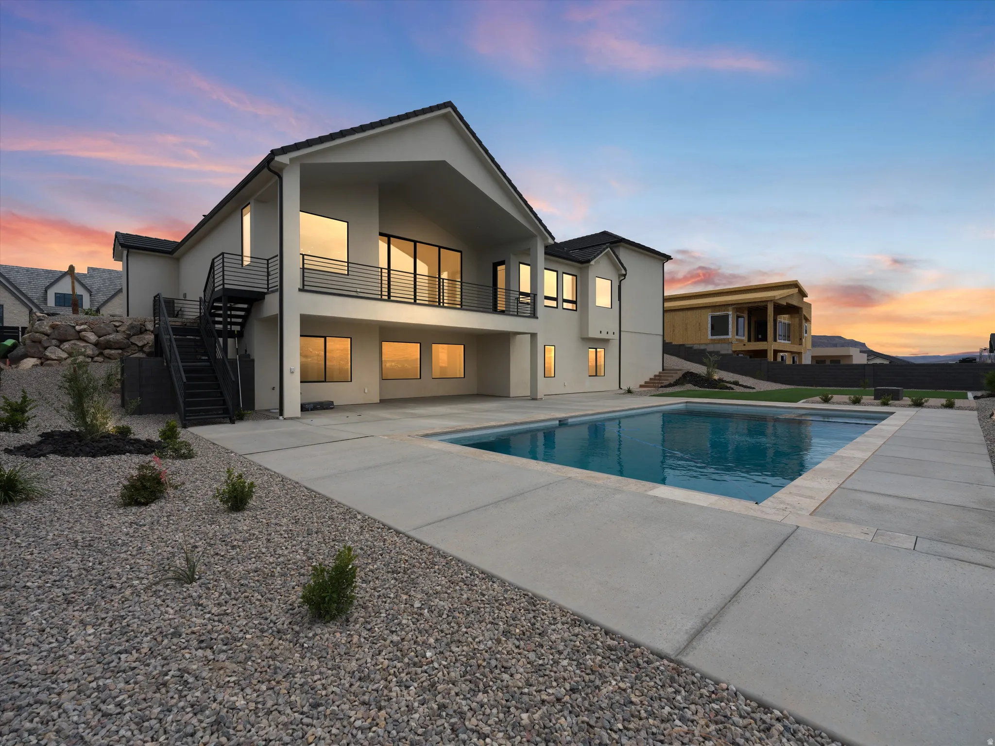 Sleek contemporary exterior featuring a private swimming pool, expansive concrete patio, and a second-story balcony with modern metal railings