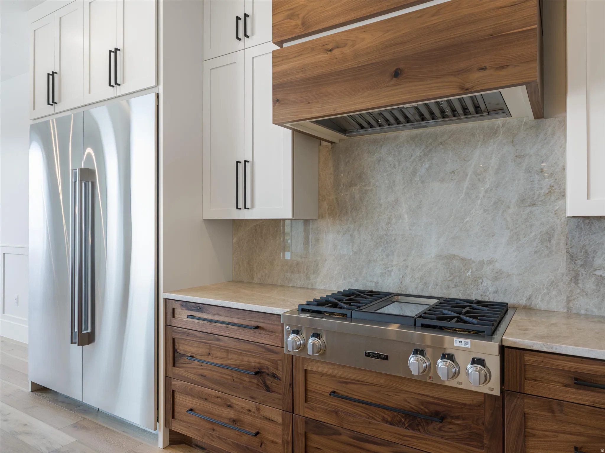 Gourmet kitchen featuring a stainless steel gas range, stone countertops, a full-height stone backsplash, custom wood cabinetry, and a wood-wrapped range hood