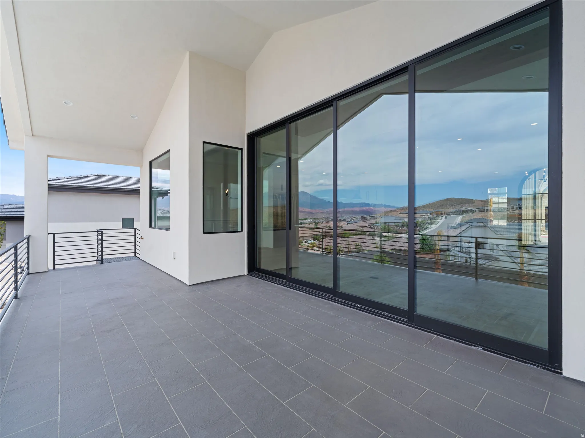 Expansive outdoor patio featuring large-format rectangular tile flooring, sleek black metal railings, and a covered ceiling with recessed lighting