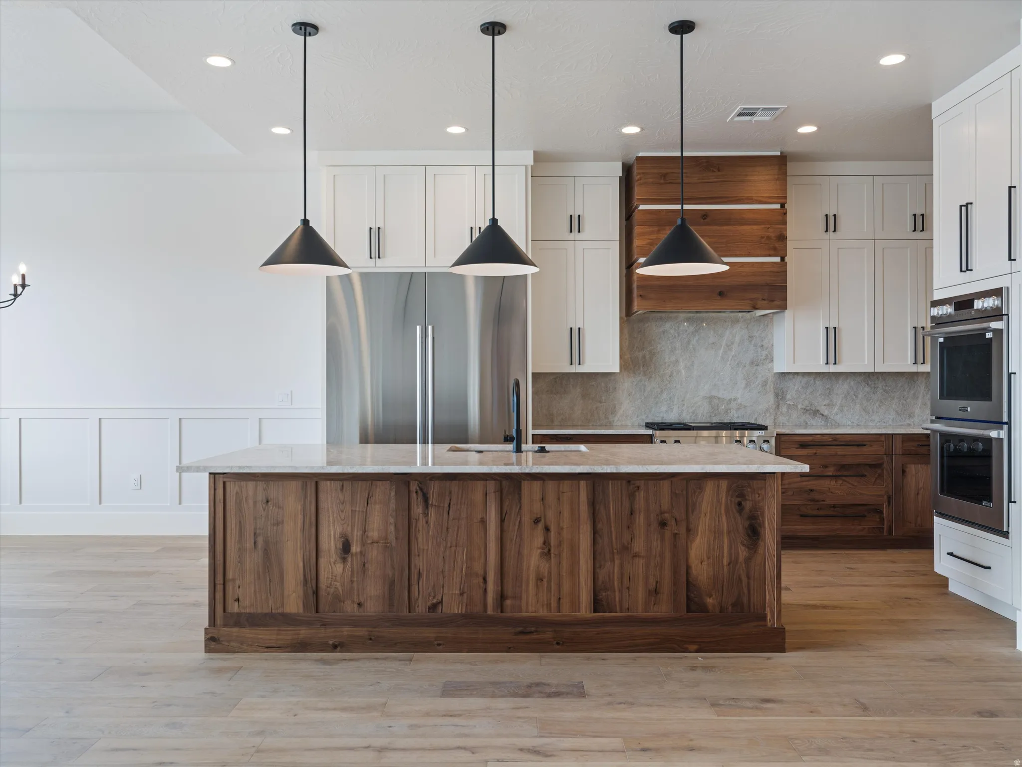 Expansive kitchen featuring a large wood-finish island with a stone-finish countertop, white upper cabinetry, and stainless steel appliances