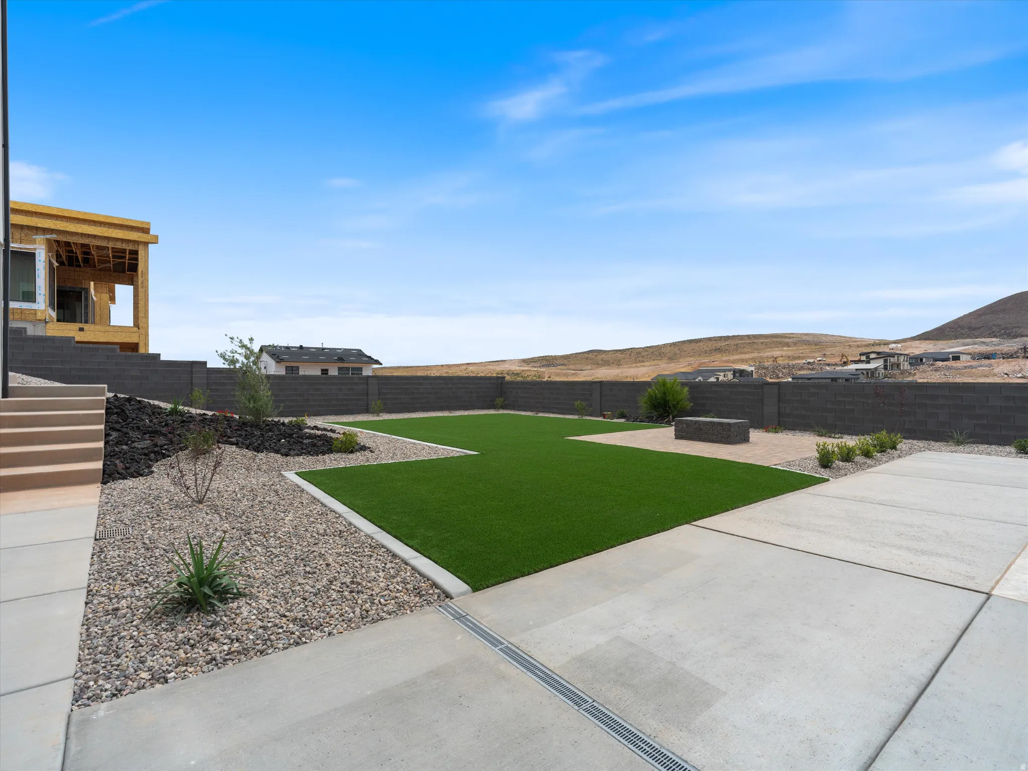 Expansive backyard featuring a large artificial turf lawn, concrete patio, and gravel landscaping