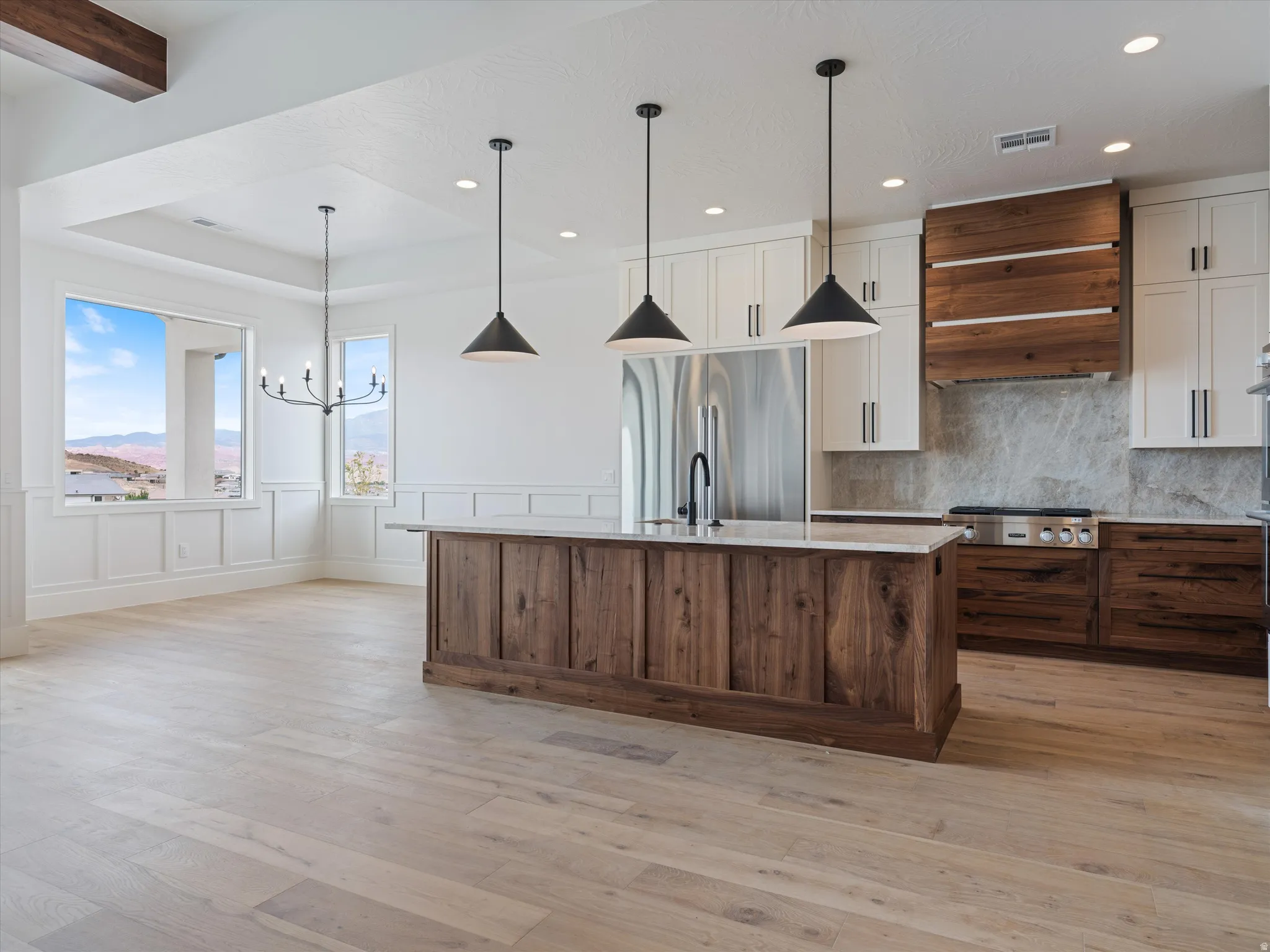 Open-concept kitchen and dining area featuring a large center island with a light-toned countertop, a stainless steel refrigerator, and a gas range