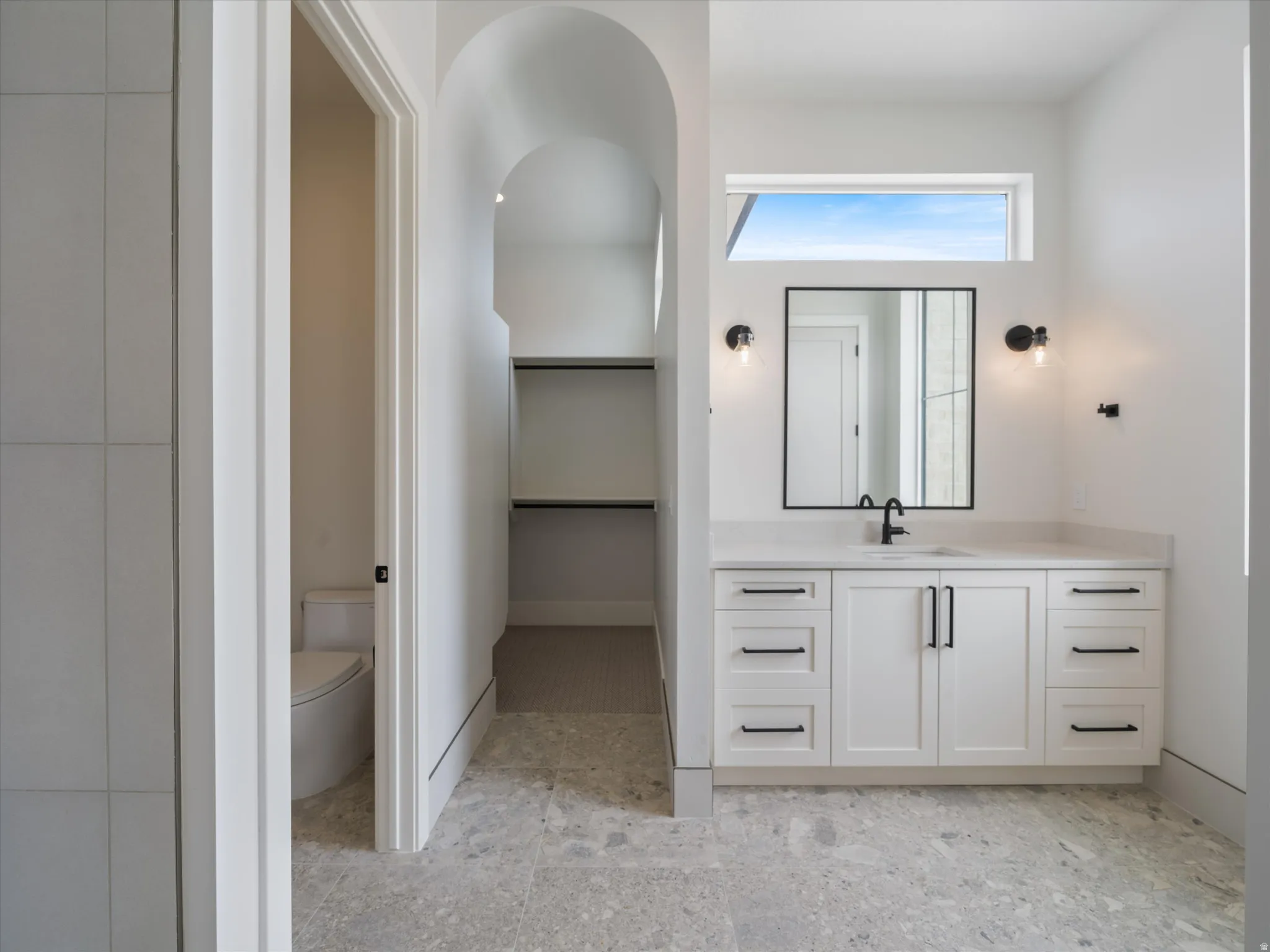White shaker-style vanity with dark hardware, undermount sink, and black wall-mounted faucet