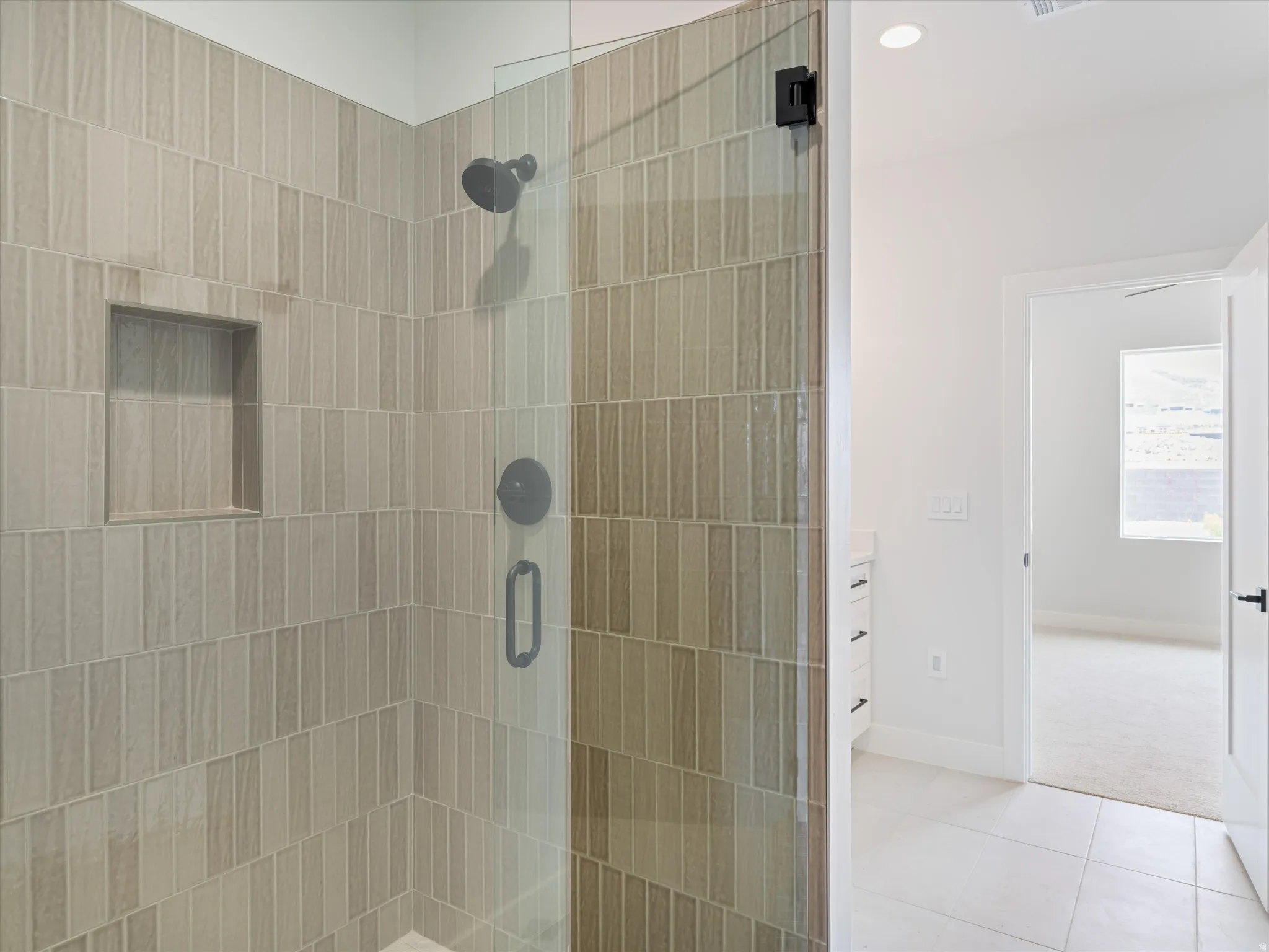 Glass-enclosed shower with vertical tile detailing, matte black fixtures, and a recessed tile niche