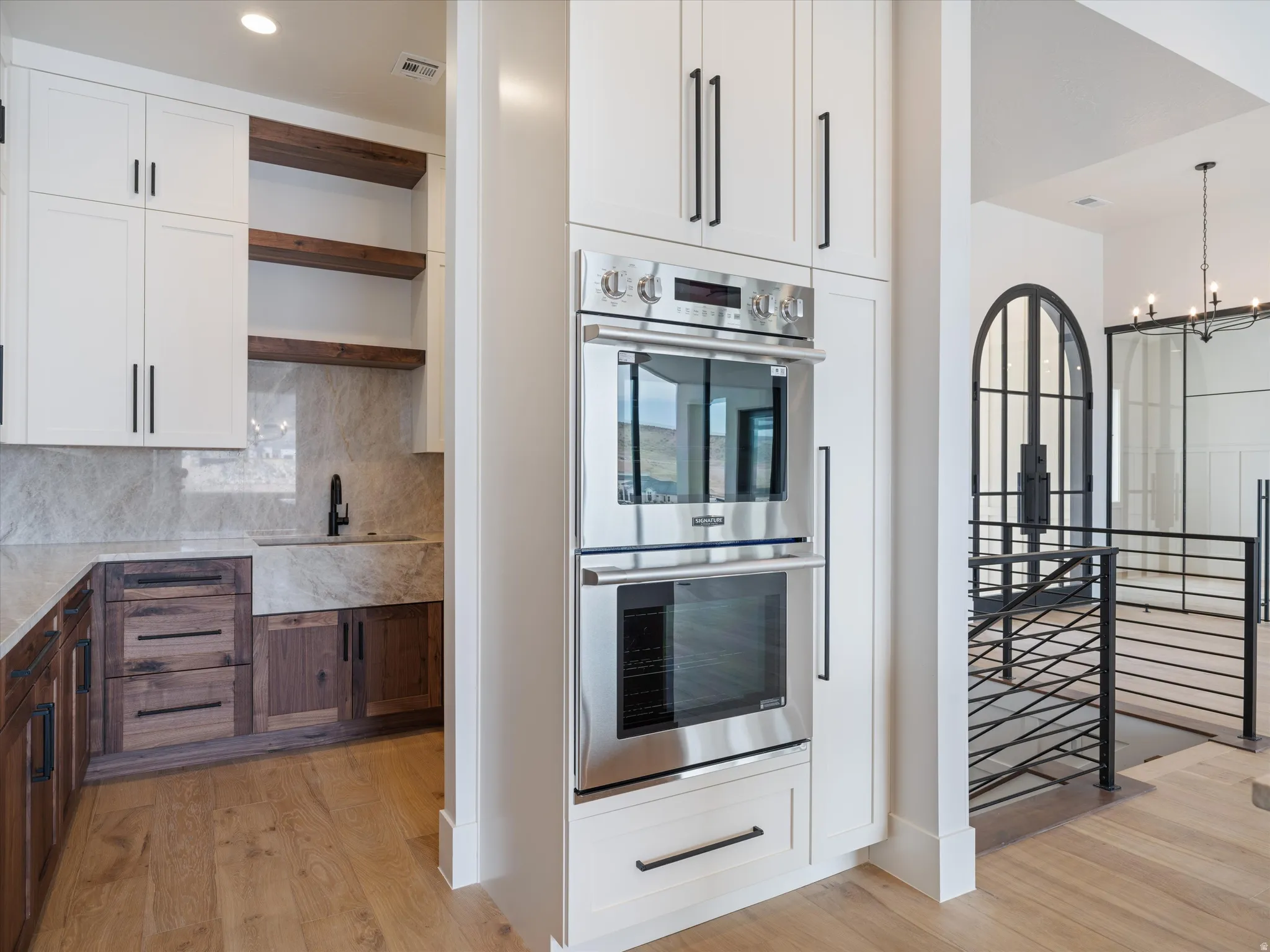 Gourmet kitchen featuring a built-in stainless steel oven and microwave, contrasting white and wood-finish cabinetry, a large farmhouse sink with a matte black faucet, and stone countertops