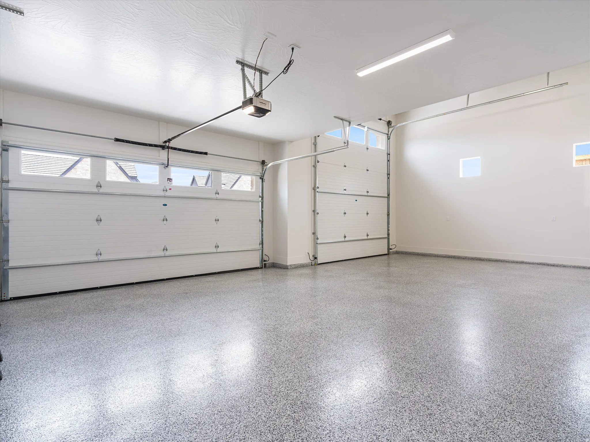 Spacious garage featuring a durable epoxy floor finish, two overhead garage doors, an automatic garage door opener, and overhead strip lighting