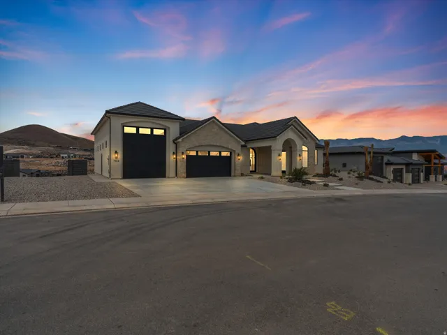 Modern desert architecture featuring a stucco and stone facade, multiple garage bays with dark doors, arched entryway, and low-maintenance landscaping