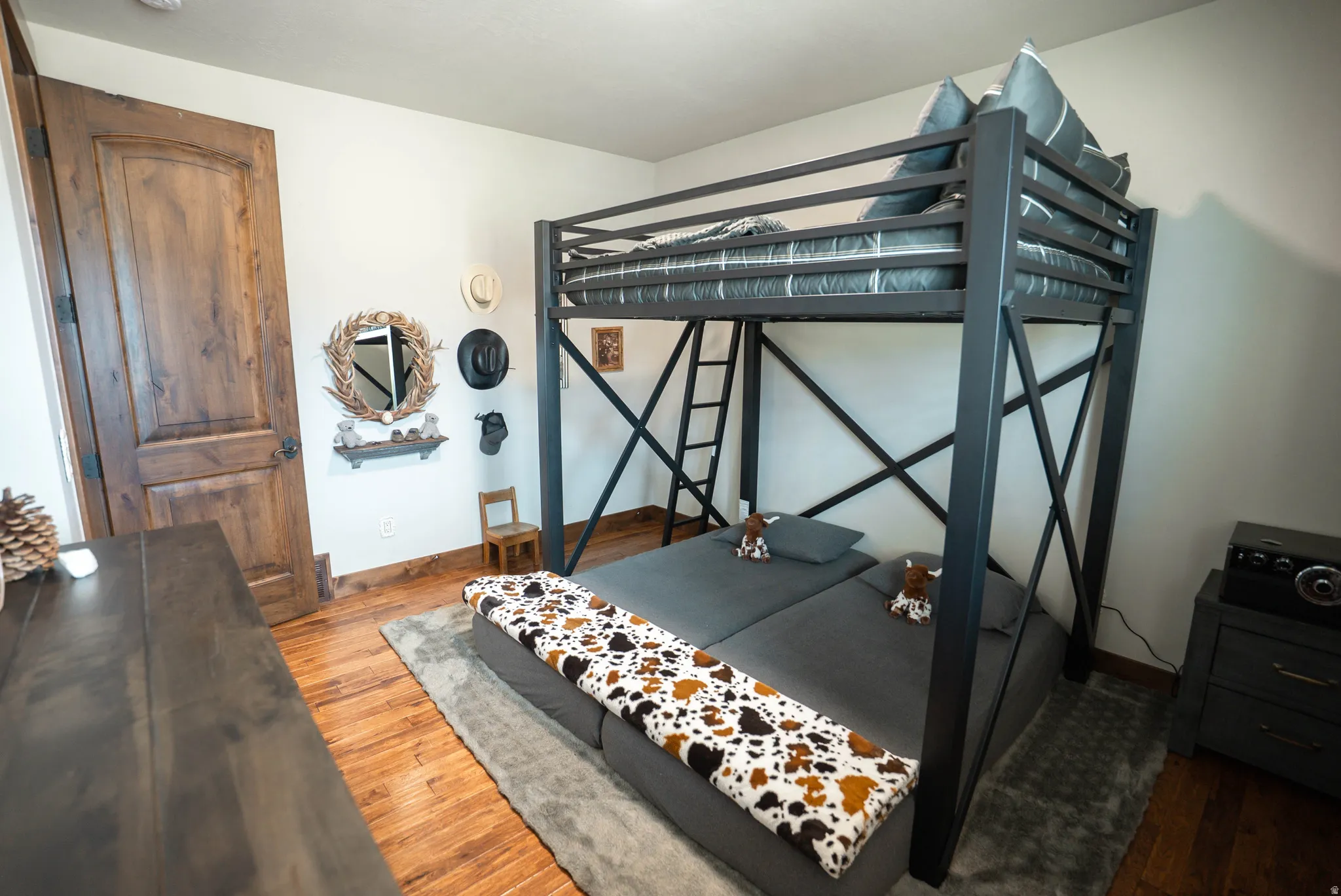 Room featuring a dark metal loft bed frame and natural wood-finish flooring