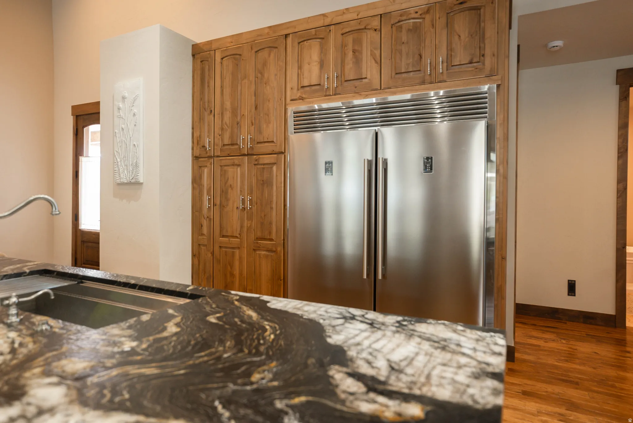 Gourmet kitchen featuring a built-in stainless steel refrigerator, extensive wood cabinetry, and a dark stone countertop with integrated sink and chrome faucet