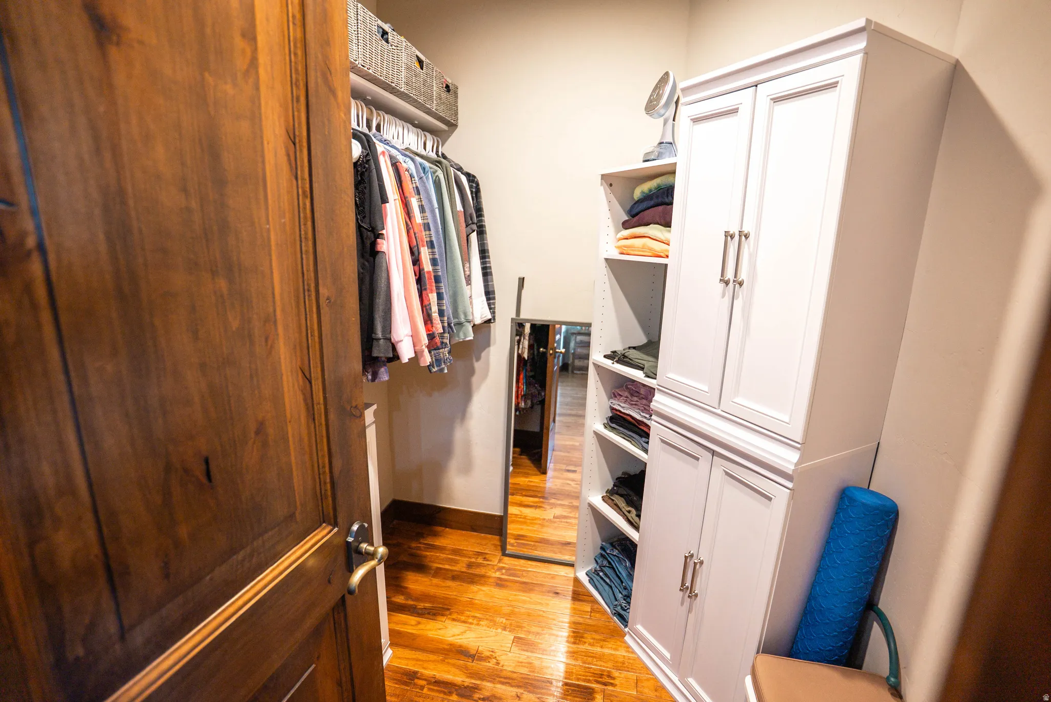 Custom built-in closet system featuring hardwood flooring, a dark wood-paneled door with bronze hardware, white cabinetry, and open shelving