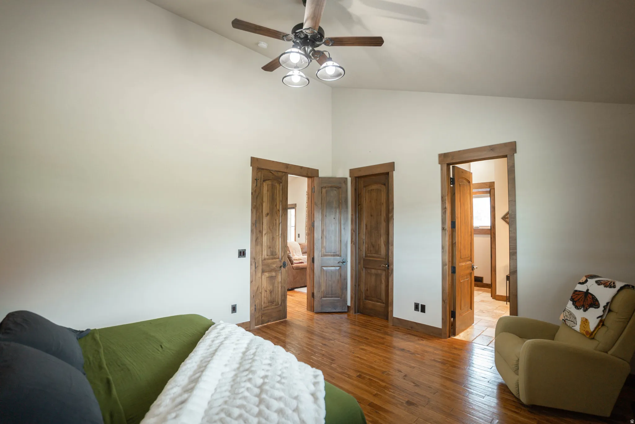 Vaulted white ceiling with a ceiling fan, wood-finish flooring, and natural wood doors