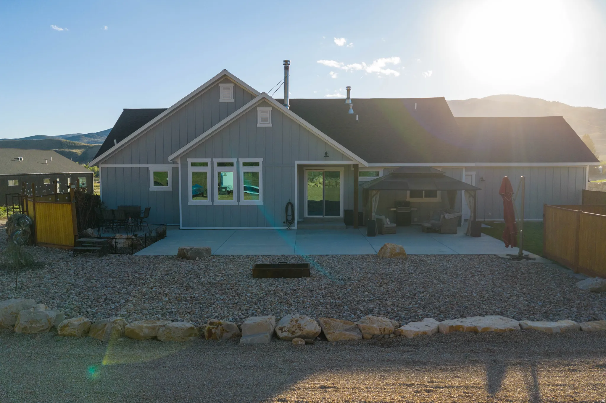 Rear exterior featuring board and batten siding, black roofing, an expansive concrete patio, and a gravel landscape