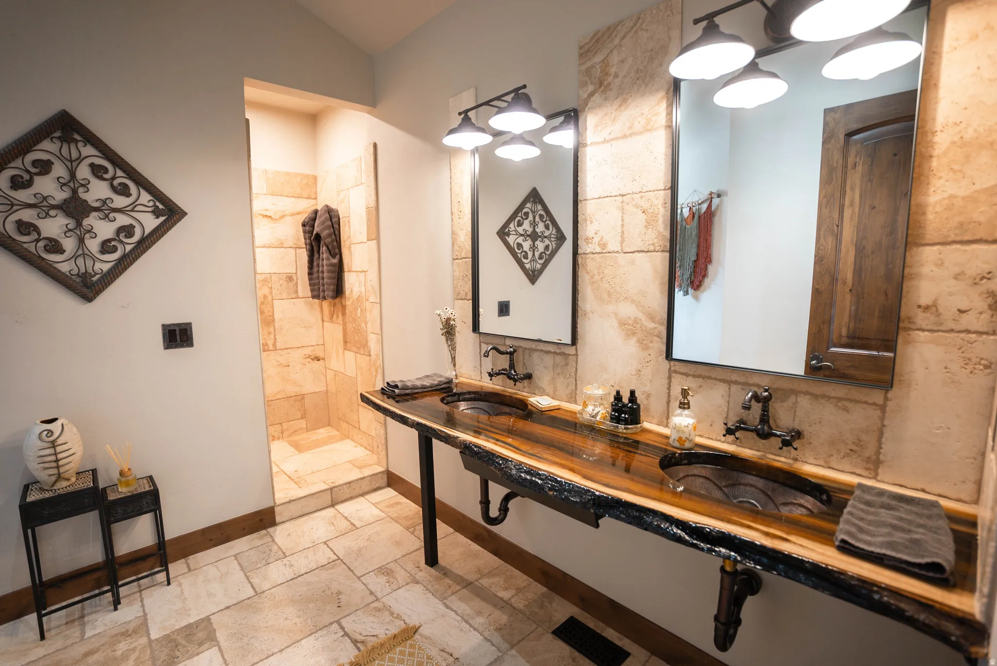 Bathroom featuring a live-edge wood vanity with dual vessel sinks, stone tile flooring, a walk-in shower with stone tile surround, and custom mirrors with integrated lighting