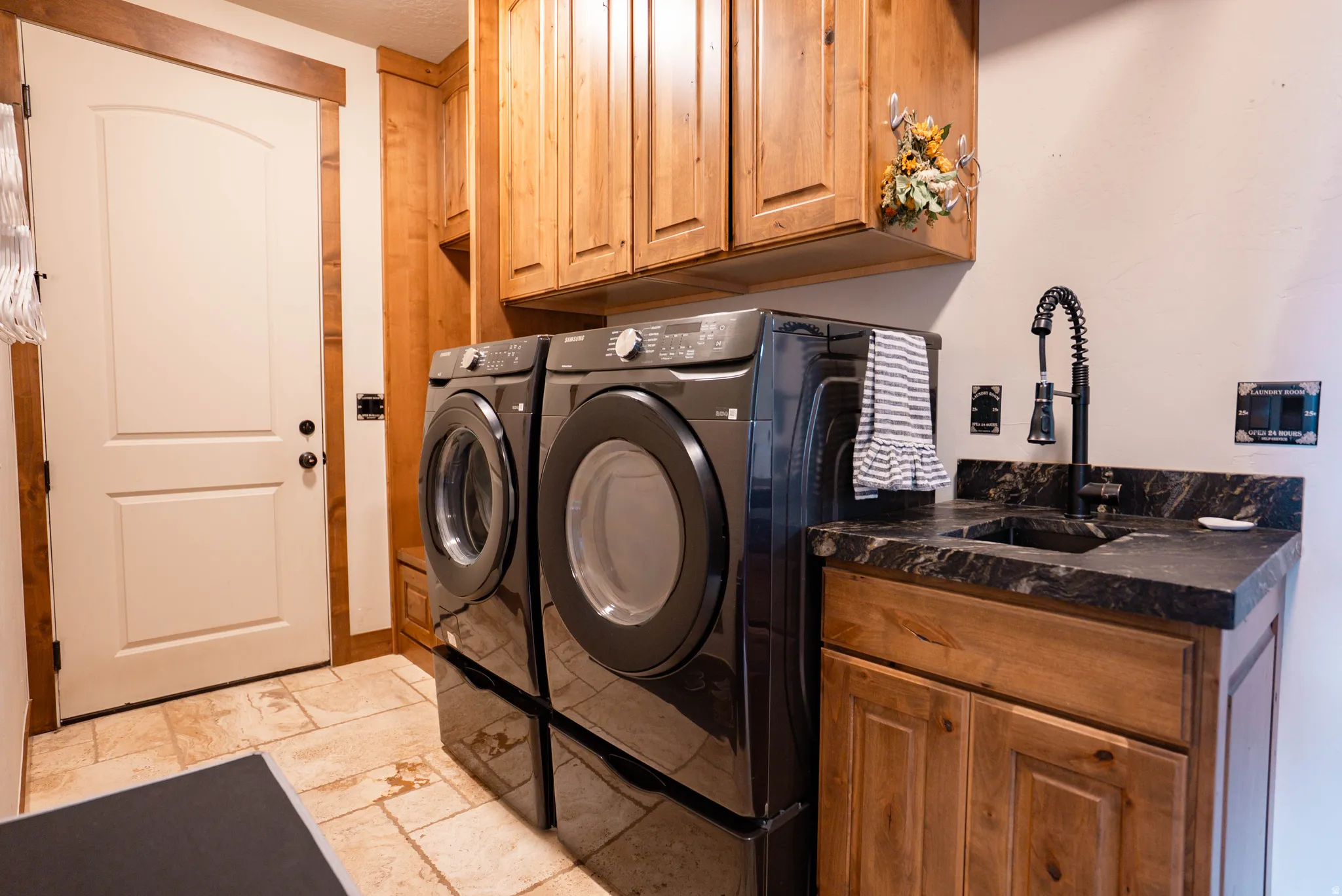 Laundry room featuring a utility sink with a matte black gooseneck faucet, light wood cabinetry, and tiled flooring