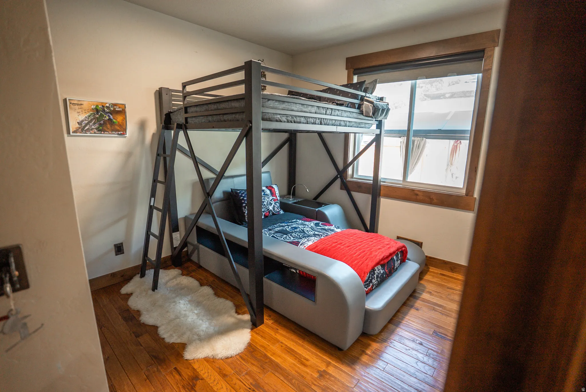 Bedroom featuring wood-finish flooring and a large window with wood trim
