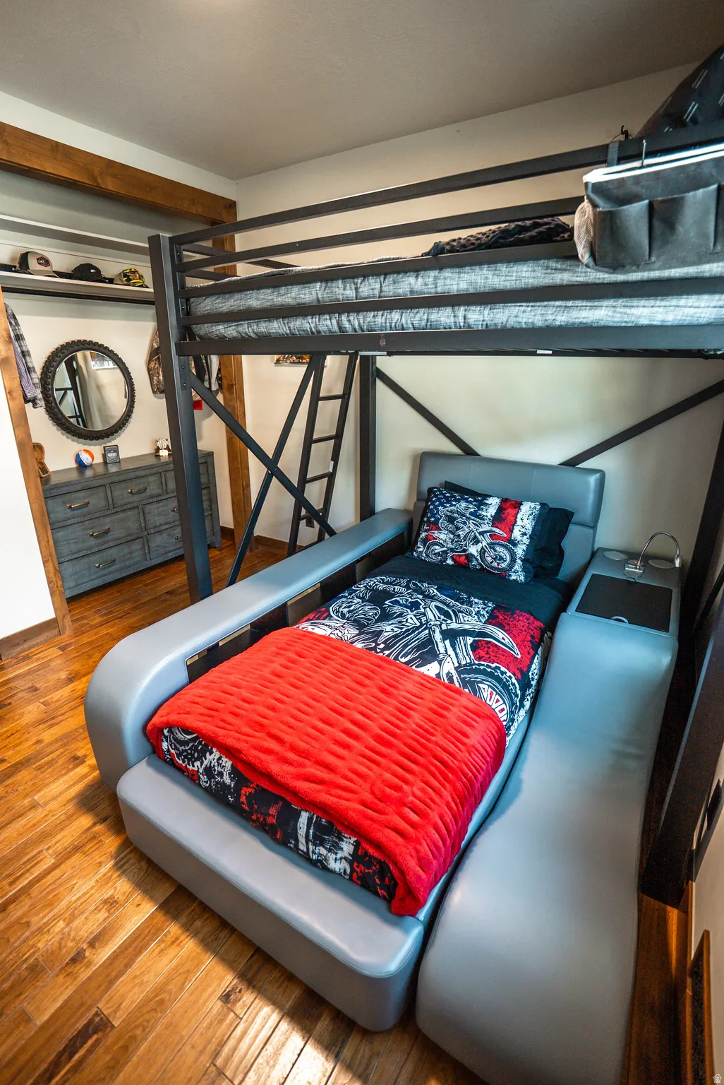 Room featuring wood-finish flooring, exposed ceiling beams, and a built-in bunk bed structure with a lower upholstered seating area